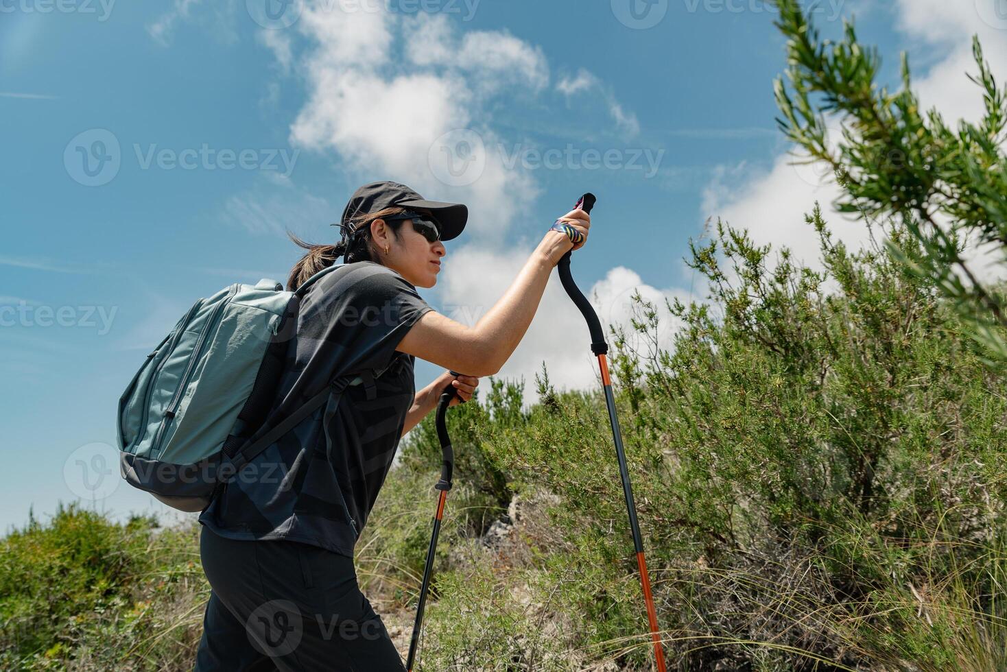 Hiker climbs the mountain supported by hiking sticks, on a sunny day and blue sky. photo