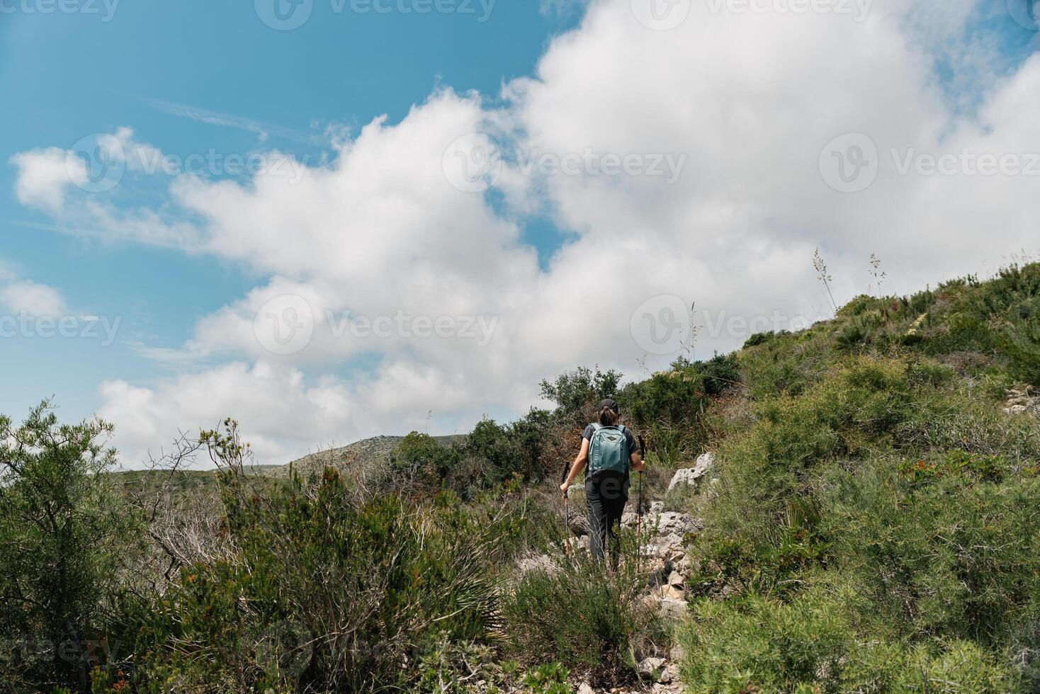 Hiker climbs the mountain surrounded by bushes with a nice blue sky with clouds. photo