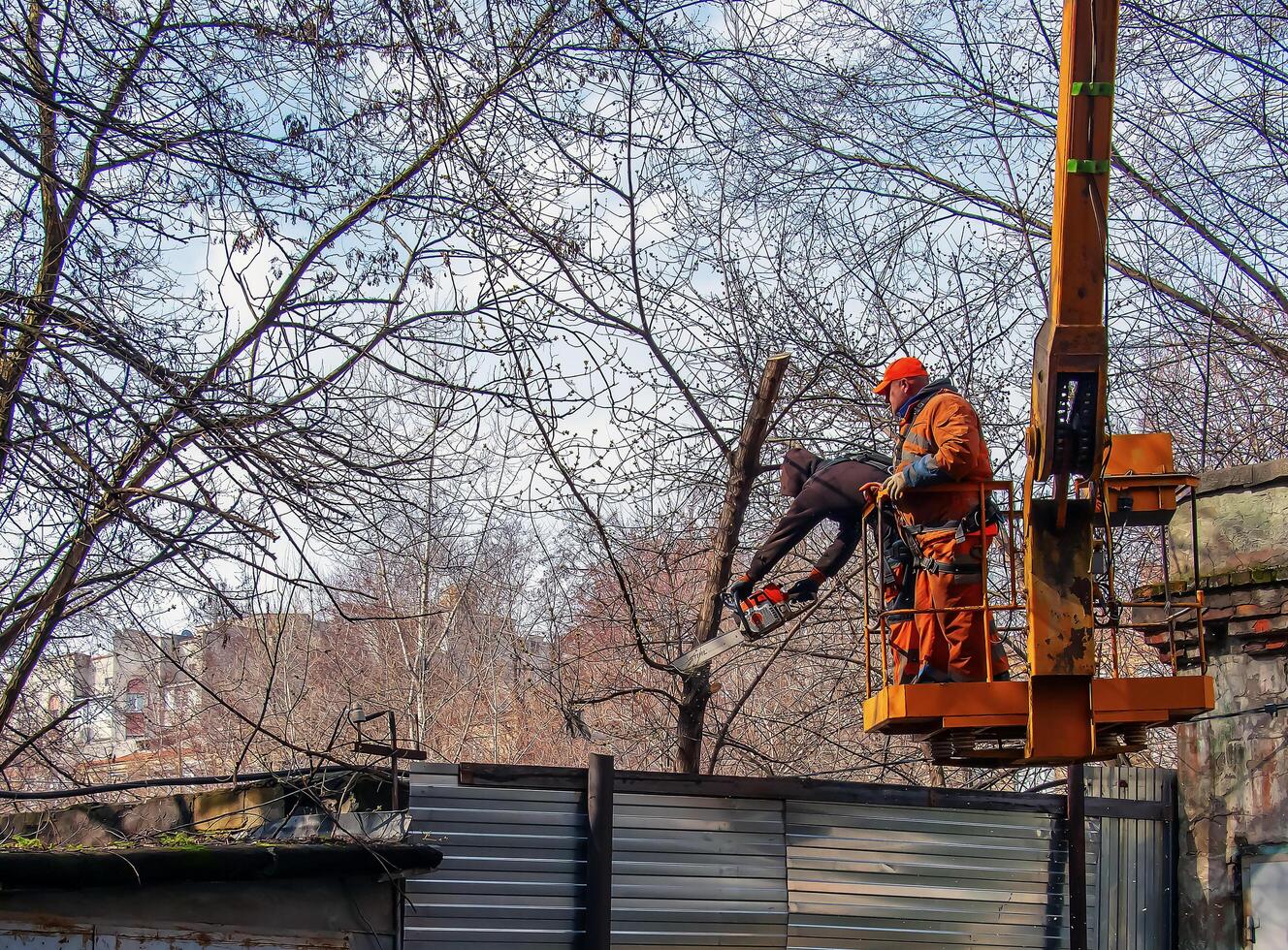 Dnepr, Ukraine - 03.20.2024 Municipal service workers stand with a chainsaw in a crane basket and trim dangerous trees photo