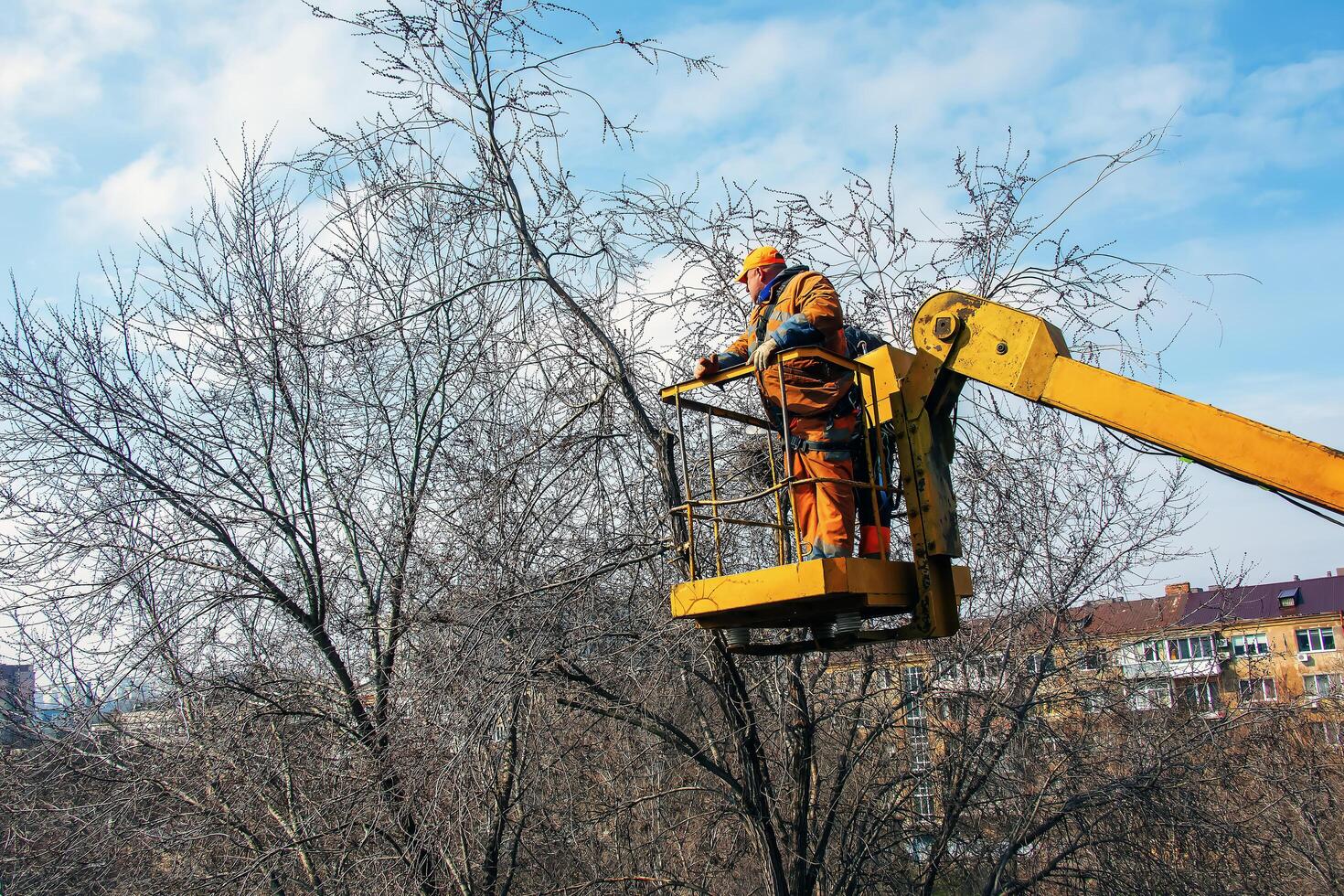 Dnepr, Ukraine - 03.20.2024 Municipal service workers stand with a chainsaw in a crane basket and trim dangerous trees photo