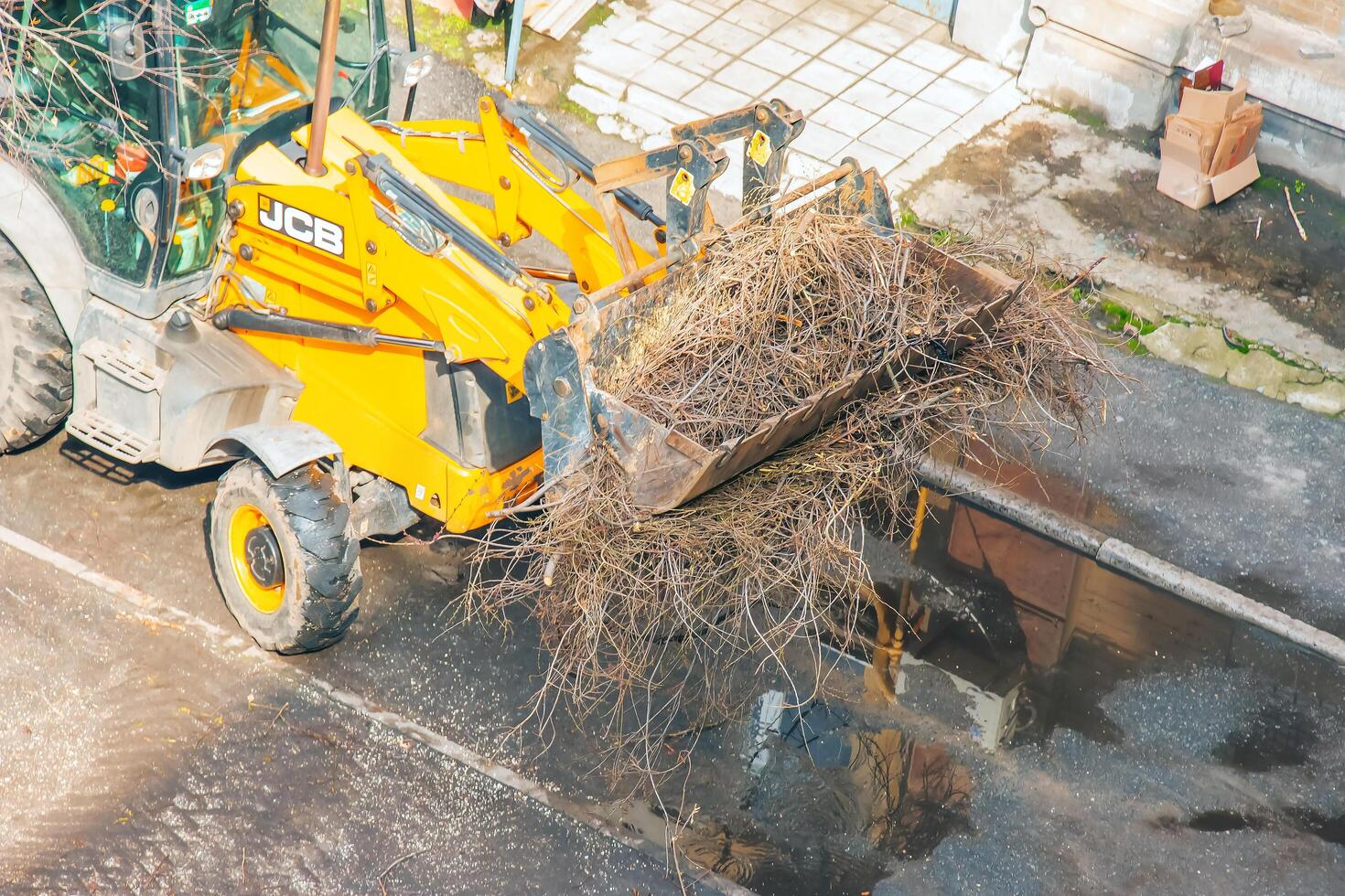 Dnepr, Ukraine - 03.20.2024 A bulldozer collects branches after pruning trees. View from above photo