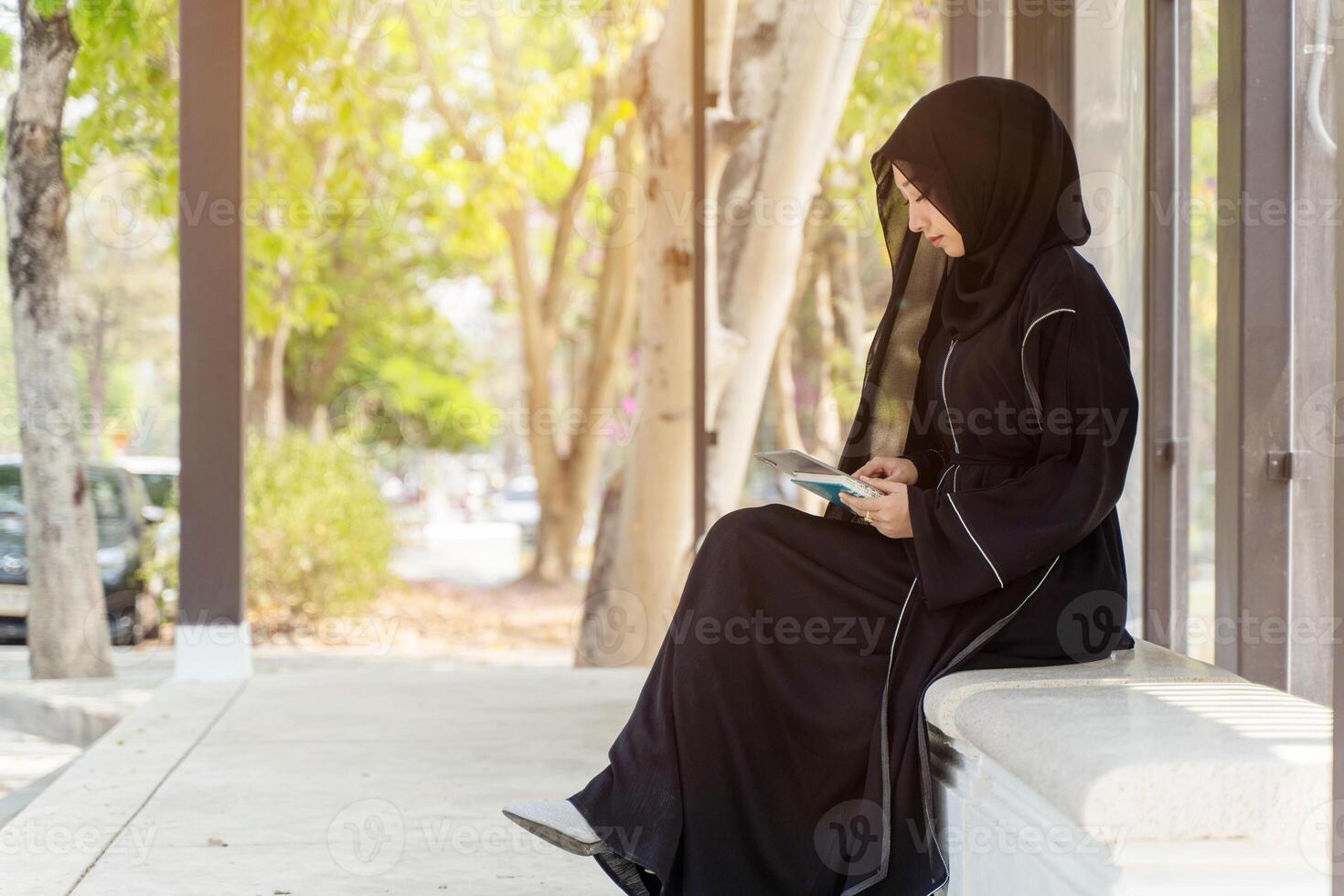 Side view of Muslim student wearing traditional clothes sit and review the lesson on tablet for the exam in university with sun fare and blurred background. photo