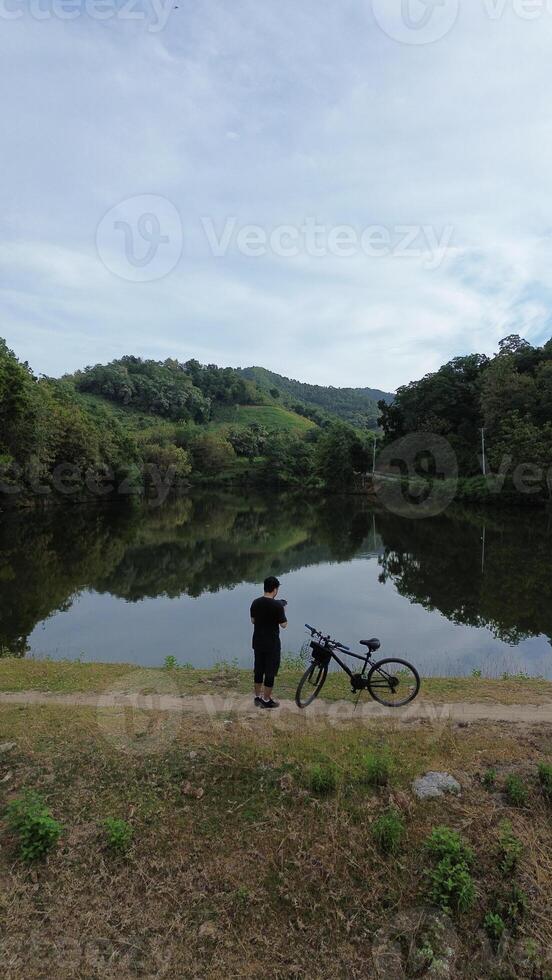 Man Resting with His Bicycle by the Lake, Enjoying the Beautiful Summer Morning Background photo