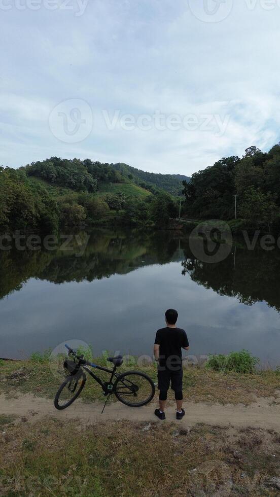 Man Resting with His Bicycle by the Lake, Enjoying the Beautiful Summer Morning Background photo
