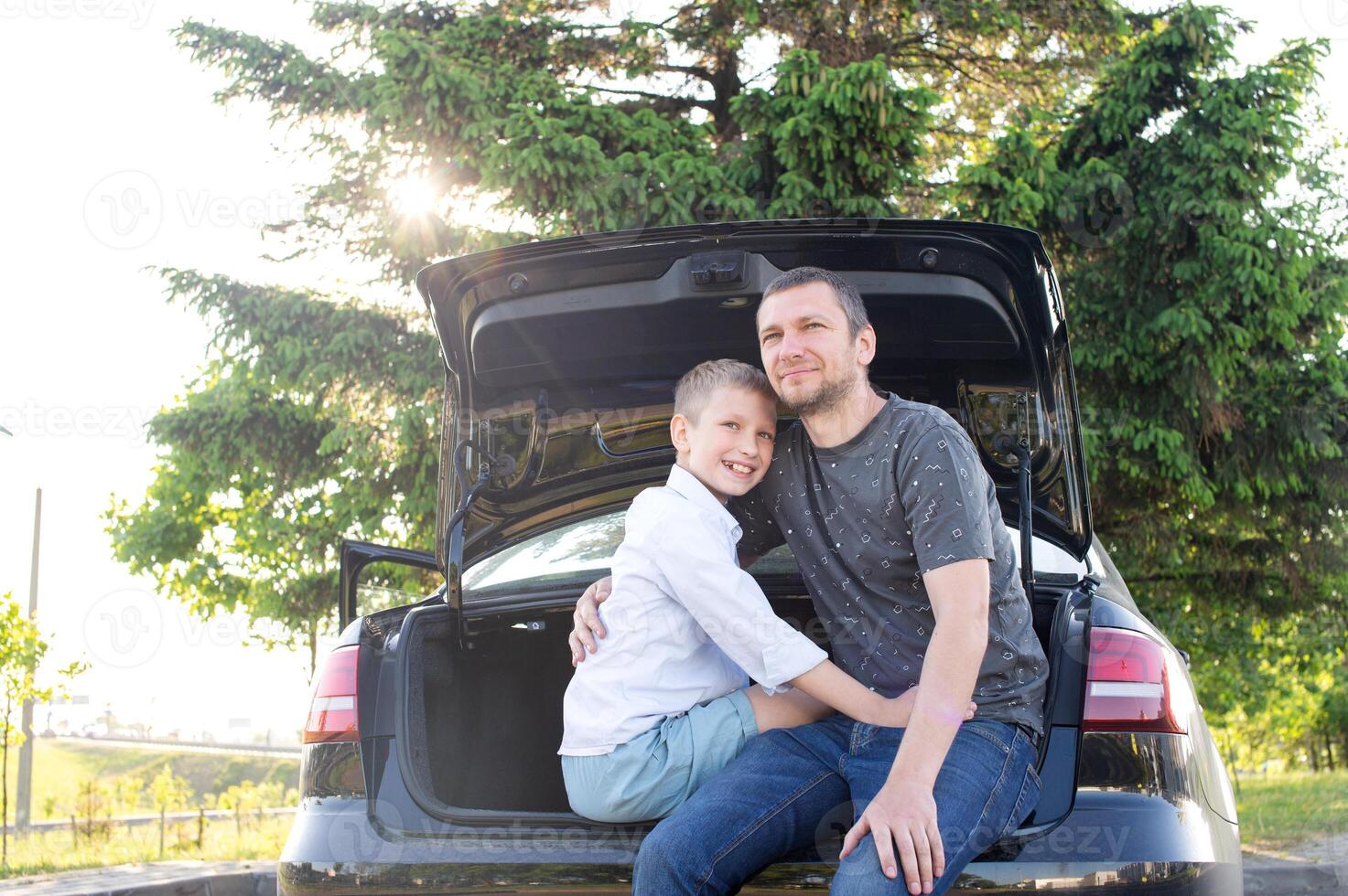 Dad and son are sitting in the trunk of a car at sunset. Hugging Dad and laughing photo
