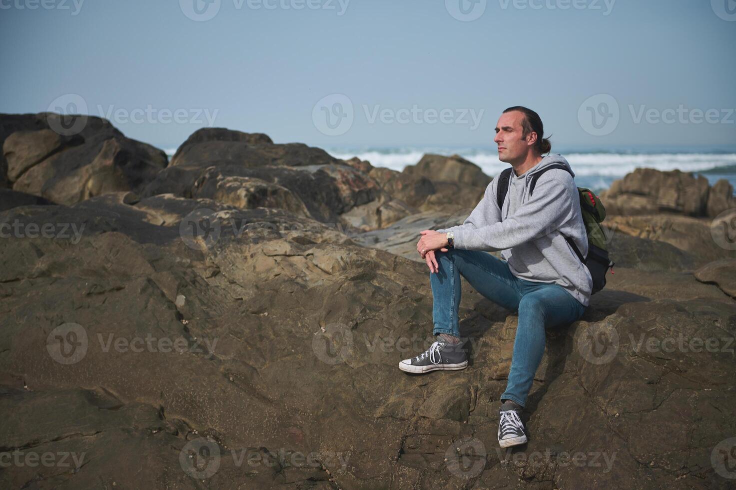 Man sitting on rocks at the beach, enjoying the ocean view and peaceful moment photo