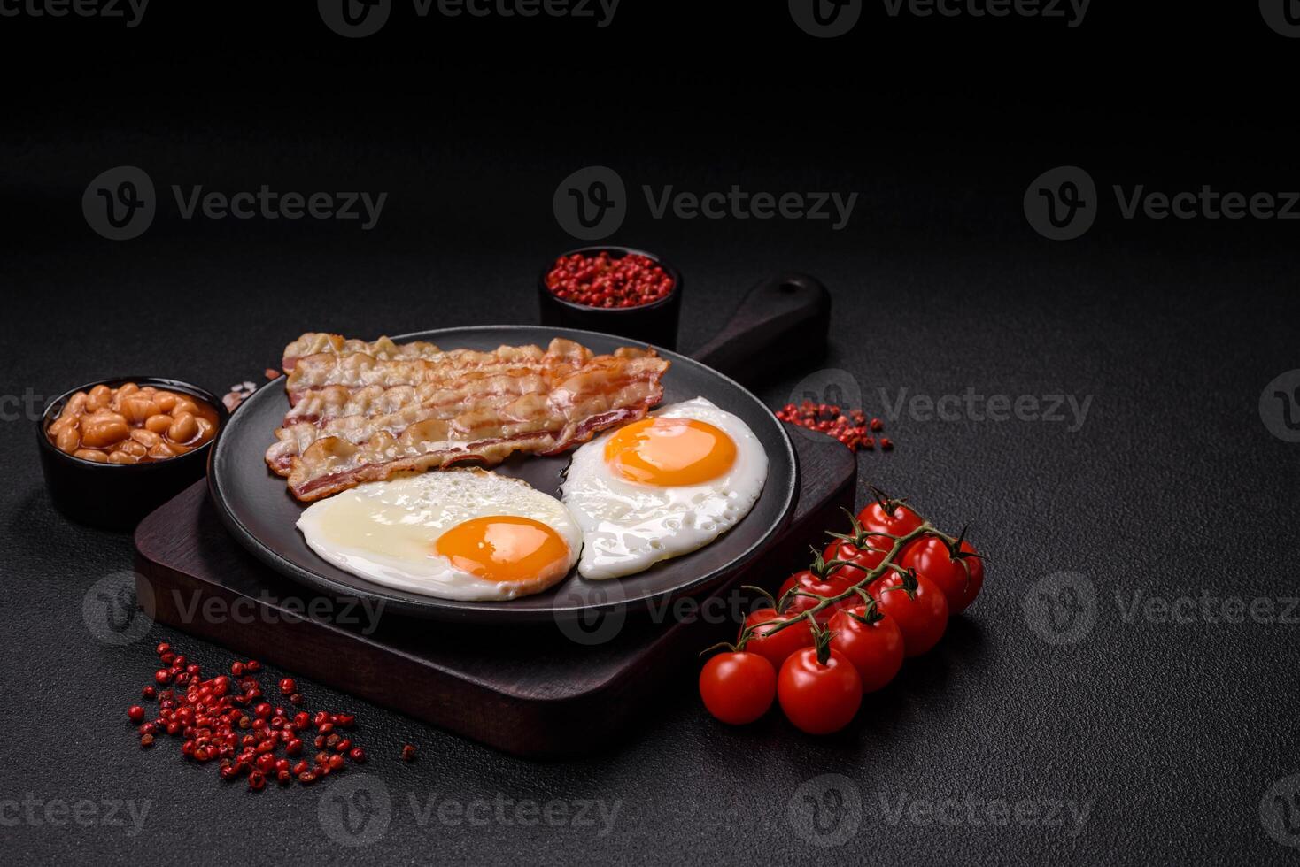 English breakfast with fried eggs, bacon, beans, tomatoes, spices and herbs photo