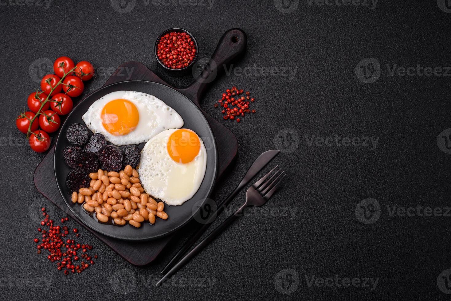 English breakfast with fried eggs, bacon, beans, tomatoes, spices and herbs photo