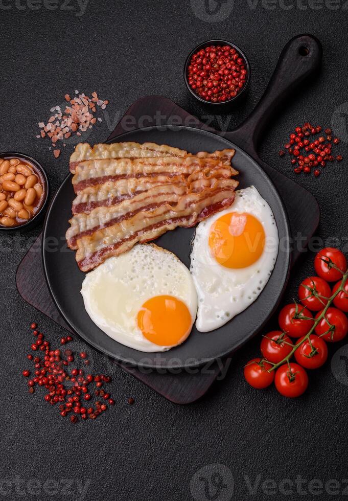 English breakfast with fried eggs, bacon, beans, tomatoes, spices and herbs photo