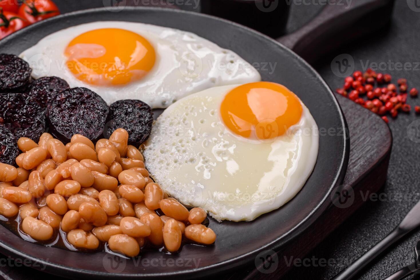 English breakfast with fried eggs, bacon, beans, tomatoes, spices and herbs photo