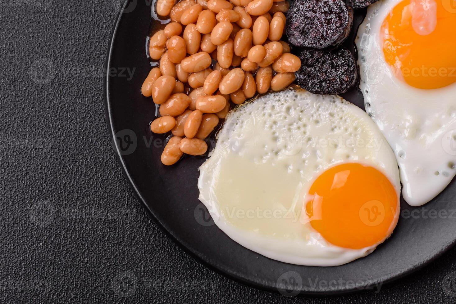 English breakfast with fried eggs, bacon, beans, tomatoes, spices and herbs photo