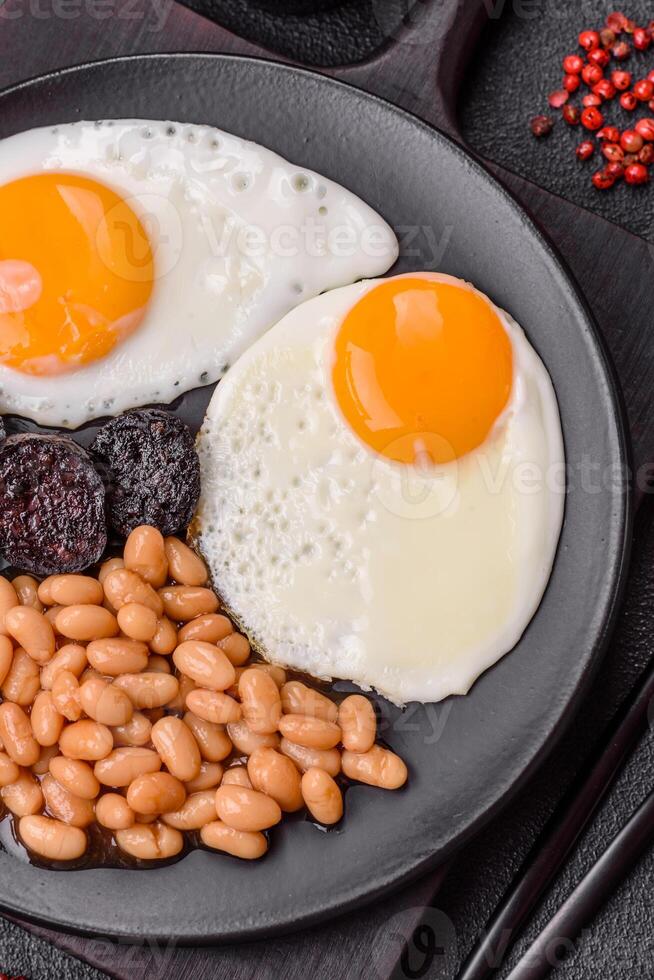English breakfast with fried eggs, bacon, beans, tomatoes, spices and herbs photo