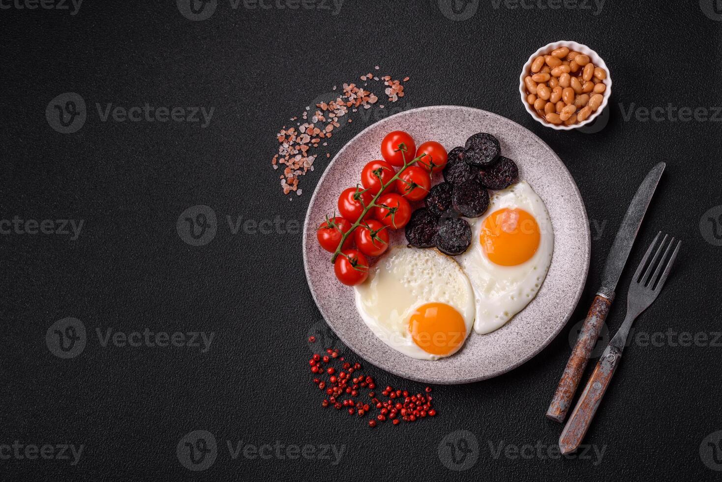English breakfast with fried eggs, bacon, beans, tomatoes, spices and herbs photo