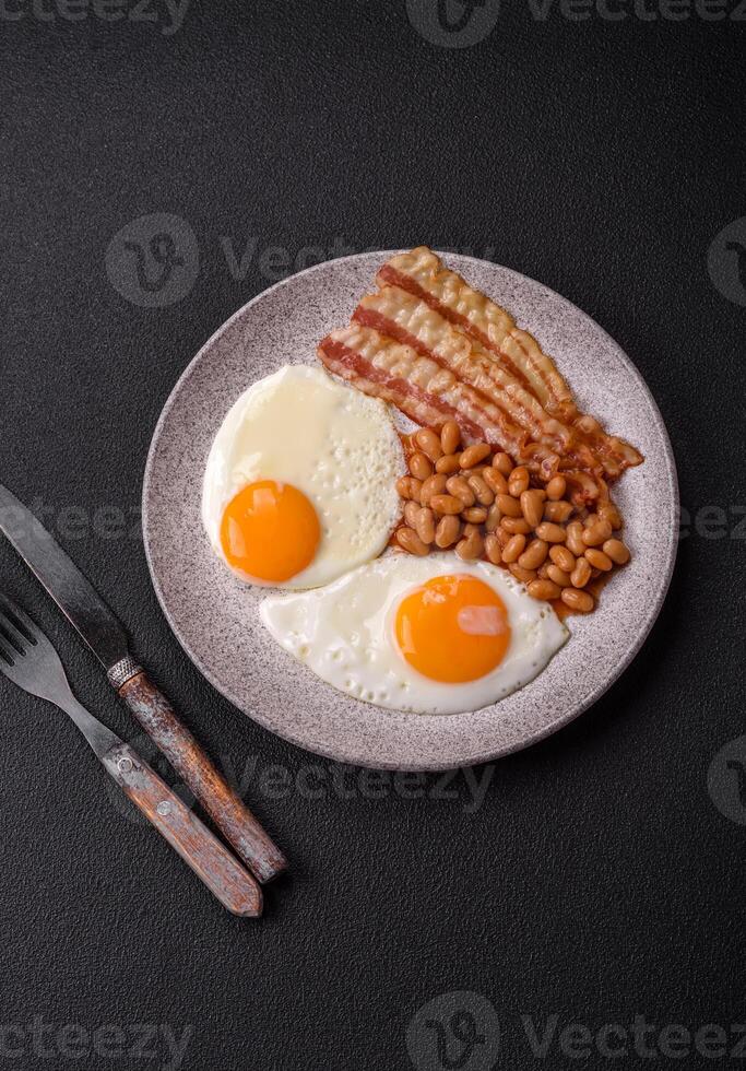 English breakfast with fried eggs, bacon, beans, tomatoes, spices and herbs photo
