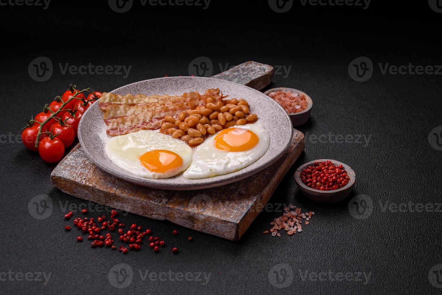 English breakfast with fried eggs, bacon, beans, tomatoes, spices and herbs photo