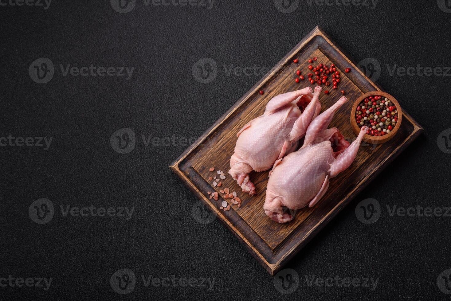 Whole raw quails with salt, spices and herbs on a dark concrete background photo