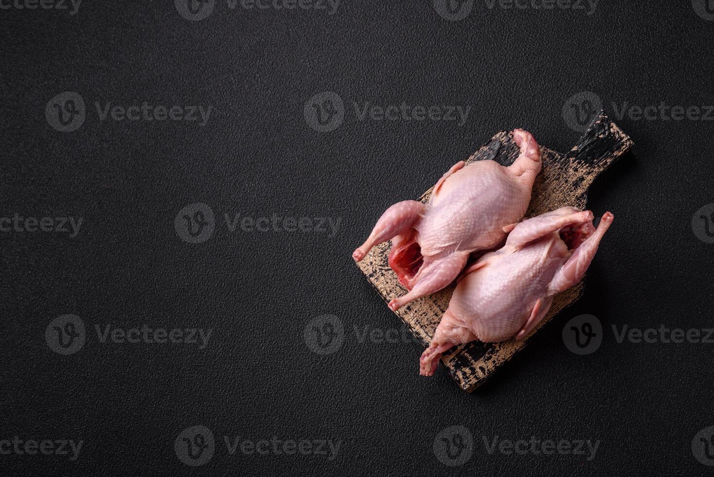 Whole raw quails with salt, spices and herbs on a dark concrete background photo