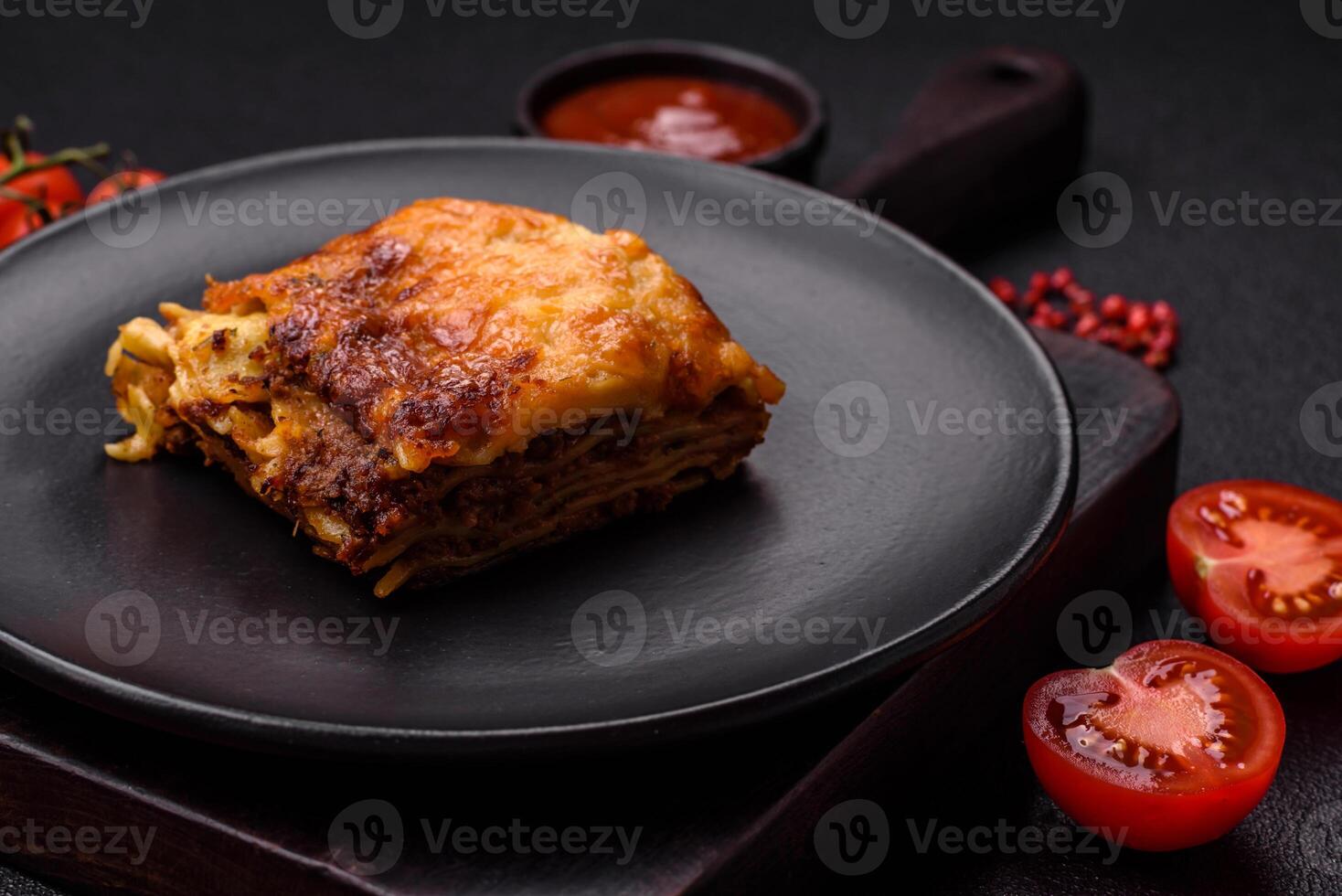 Delicious baked lasagna pasta with meat, sauce, salt, spices and herbs on a dark concrete background photo
