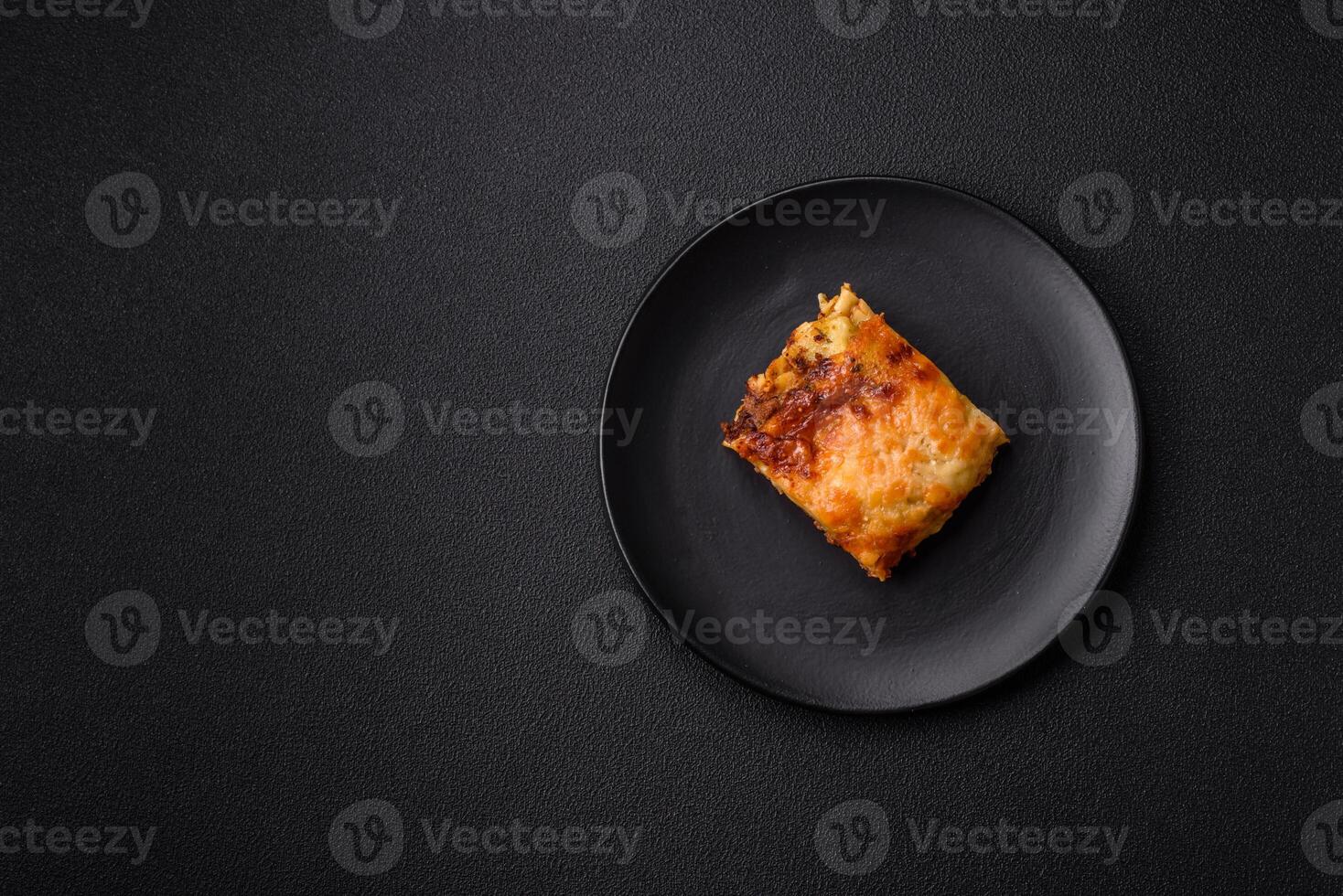Delicious baked lasagna pasta with meat, sauce, salt, spices and herbs on a dark concrete background photo