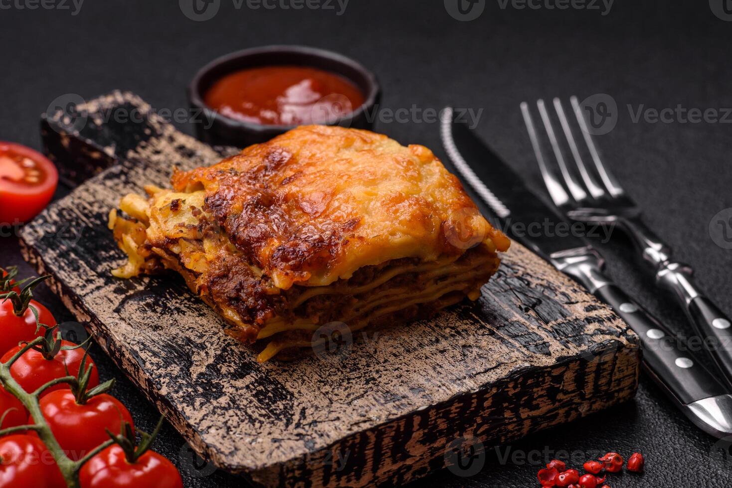 Delicious baked lasagna pasta with meat, sauce, salt, spices and herbs on a dark concrete background photo