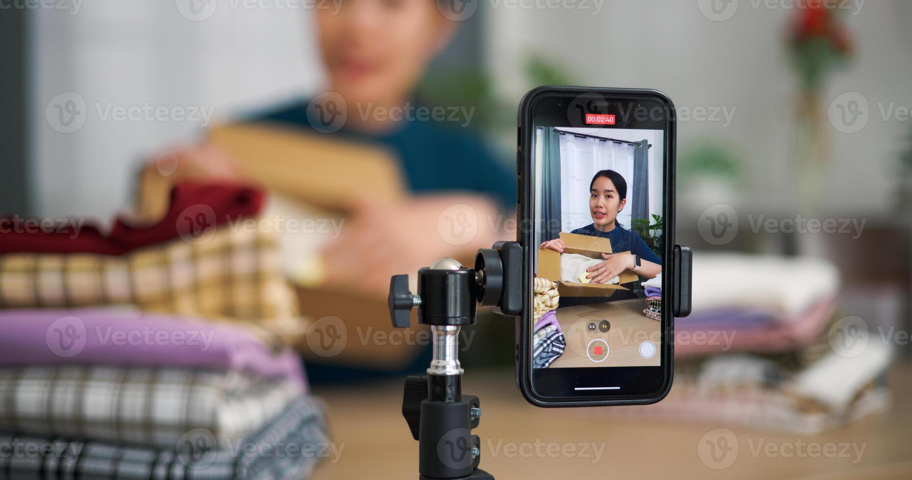 Selective focus, Young asian woman business owner selling clothes live streaming on mobile phone and packed clothes into box for a customer ,Online Shopping photo