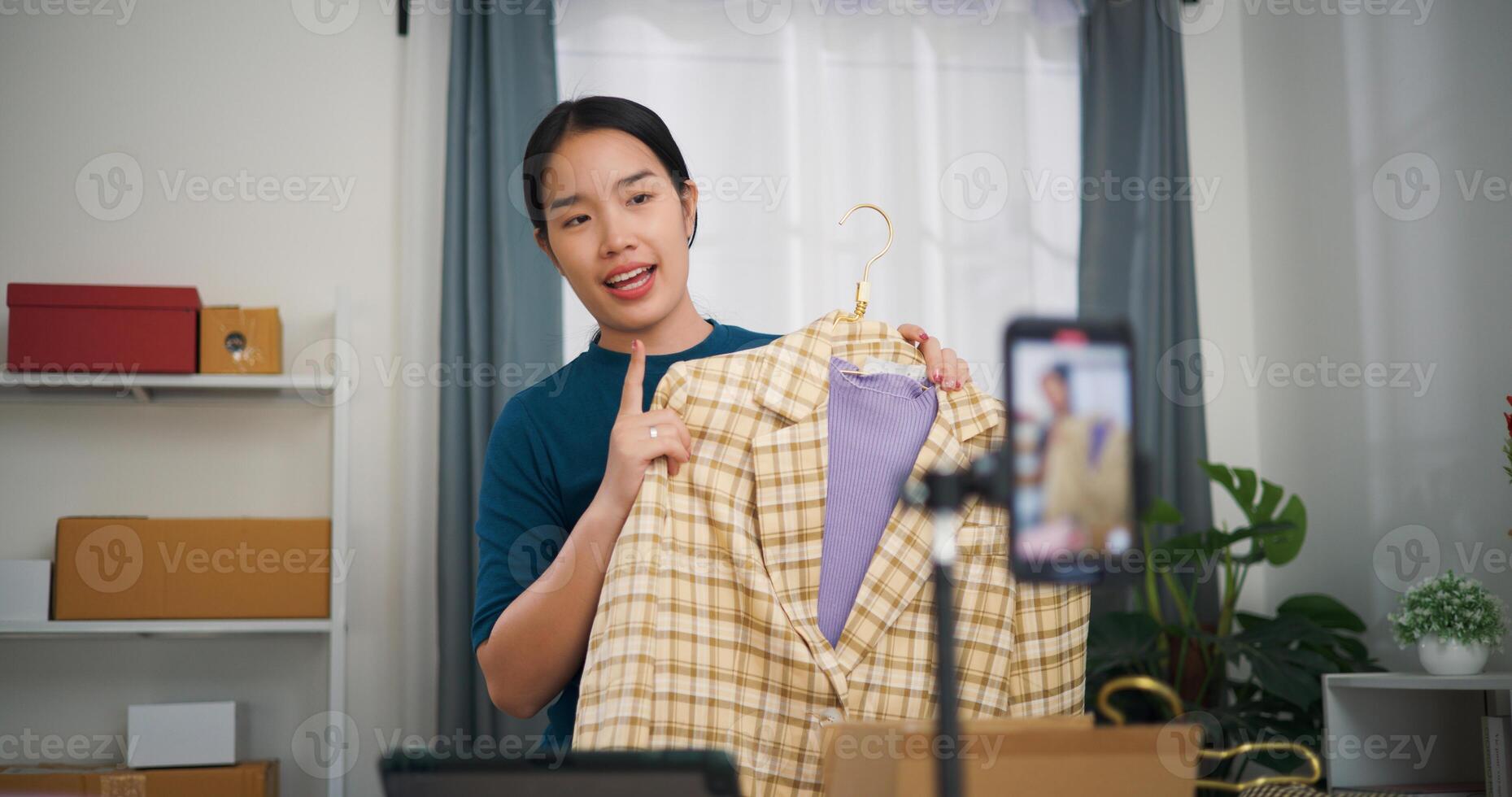 Portrait of Young asian woman business owner stand selling clothes live streaming on mobile phone show new collection fashion clothes to customer ,Online Shopping photo