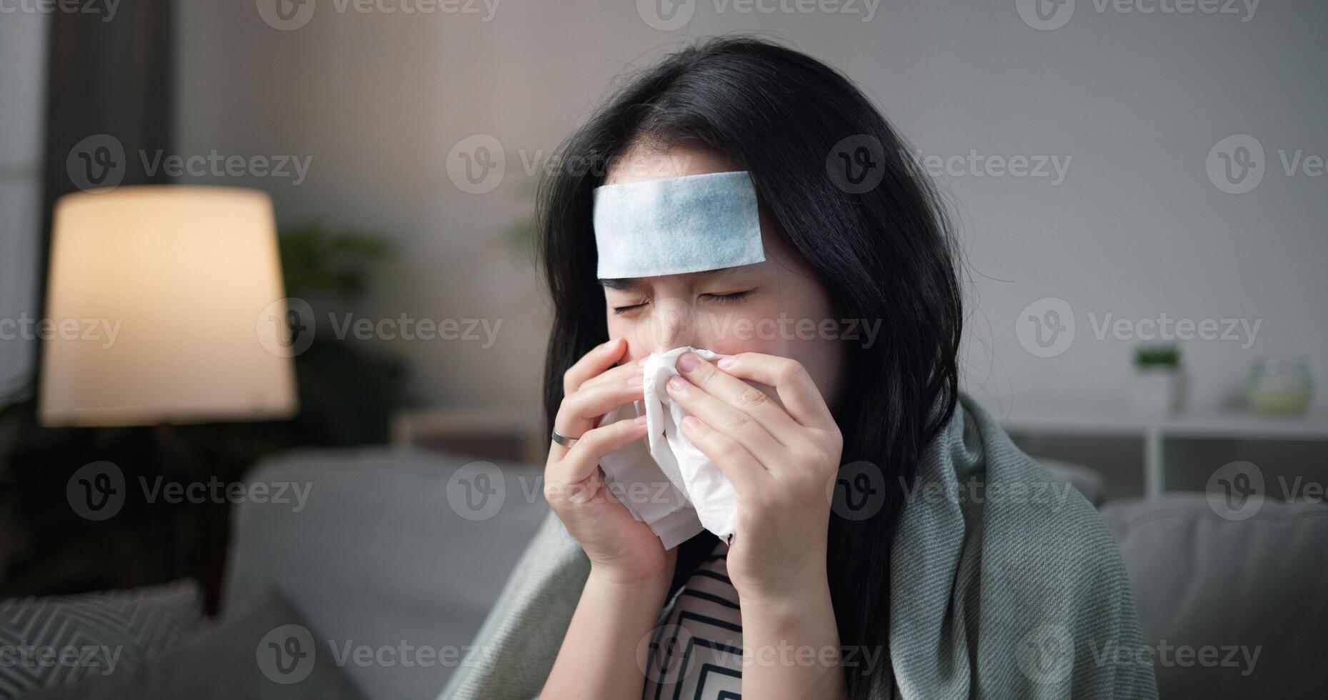 Portrait of Unwell young woman have a high fever and blowing her nose ,wrapped in blanket sitting on sofa in the living room at home, healthcare woes photo