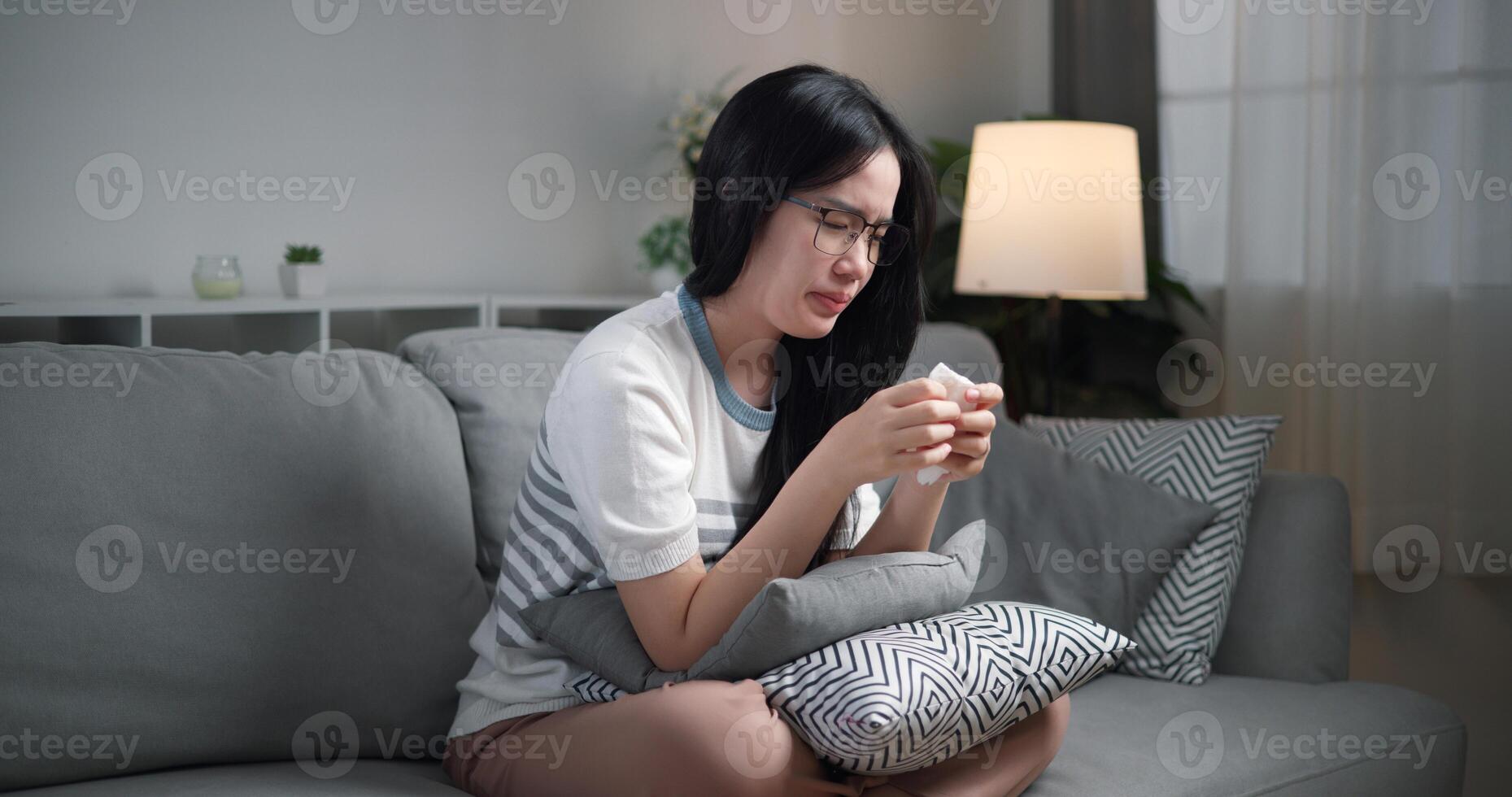 Portrait of Unwell young woman having a cold, sneezing and blowing your nose while sitting on sofa in the living room at home, healthcare woes photo