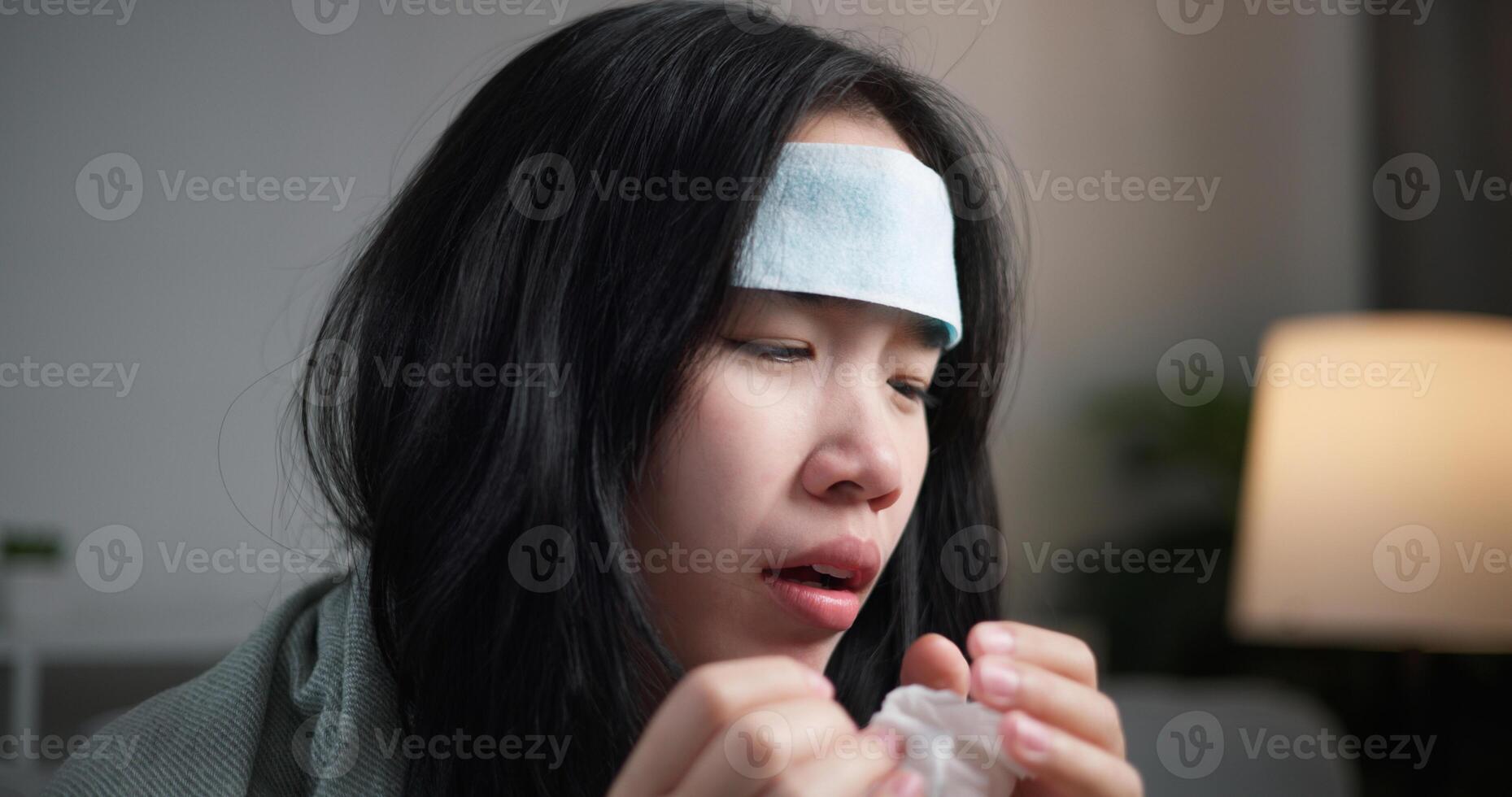 Selective focus, Unwell young woman having a cold, sneezing and blowing your nose ,wrapped in blanket sitting on sofa in the living room at home, healthcare woes photo