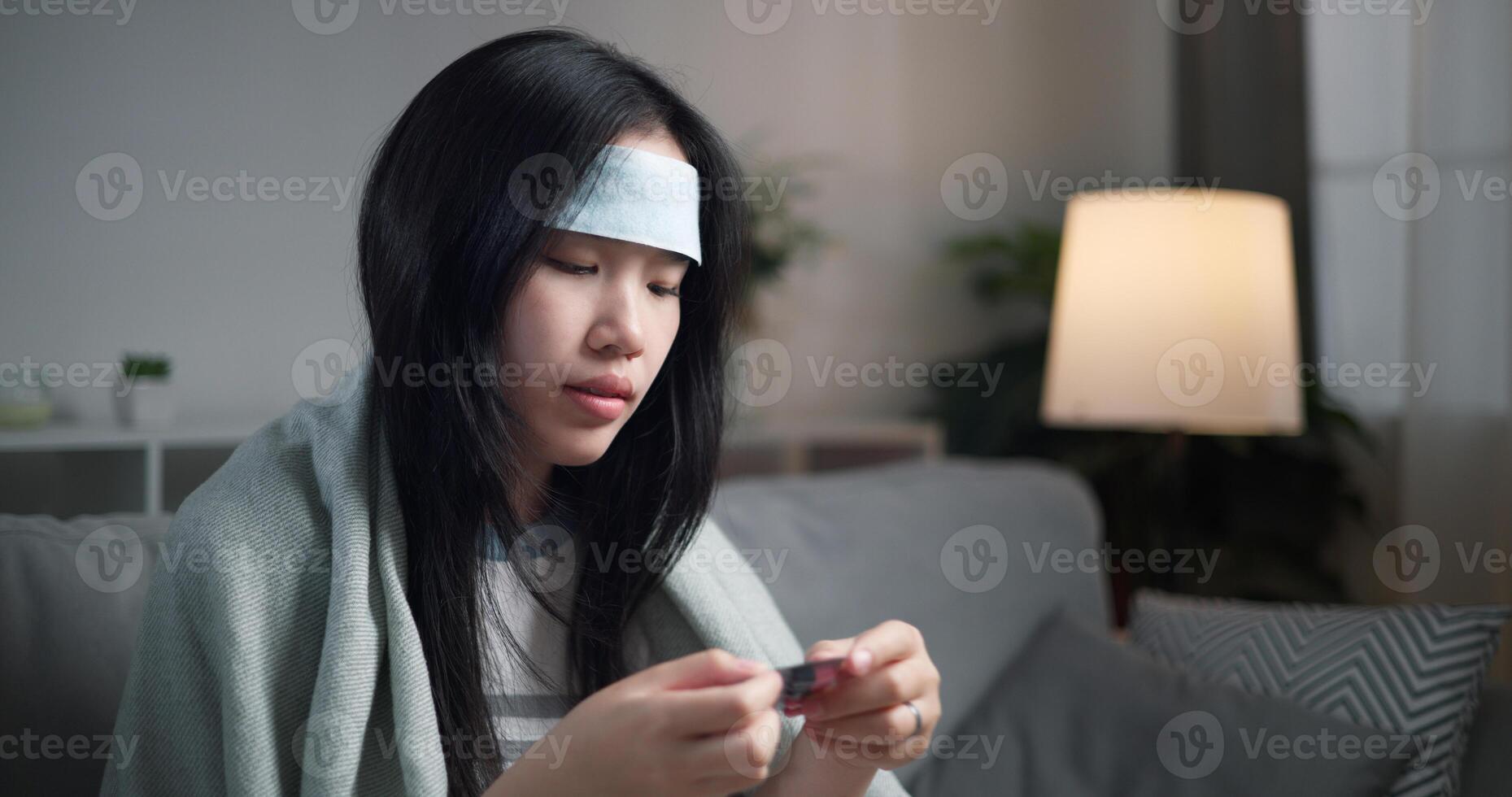 Portrait of Unwell young woman have a high fever unpacking medicine to eat ,wrapped in blanket sitting on sofa in the living room at home, healthcare woes photo
