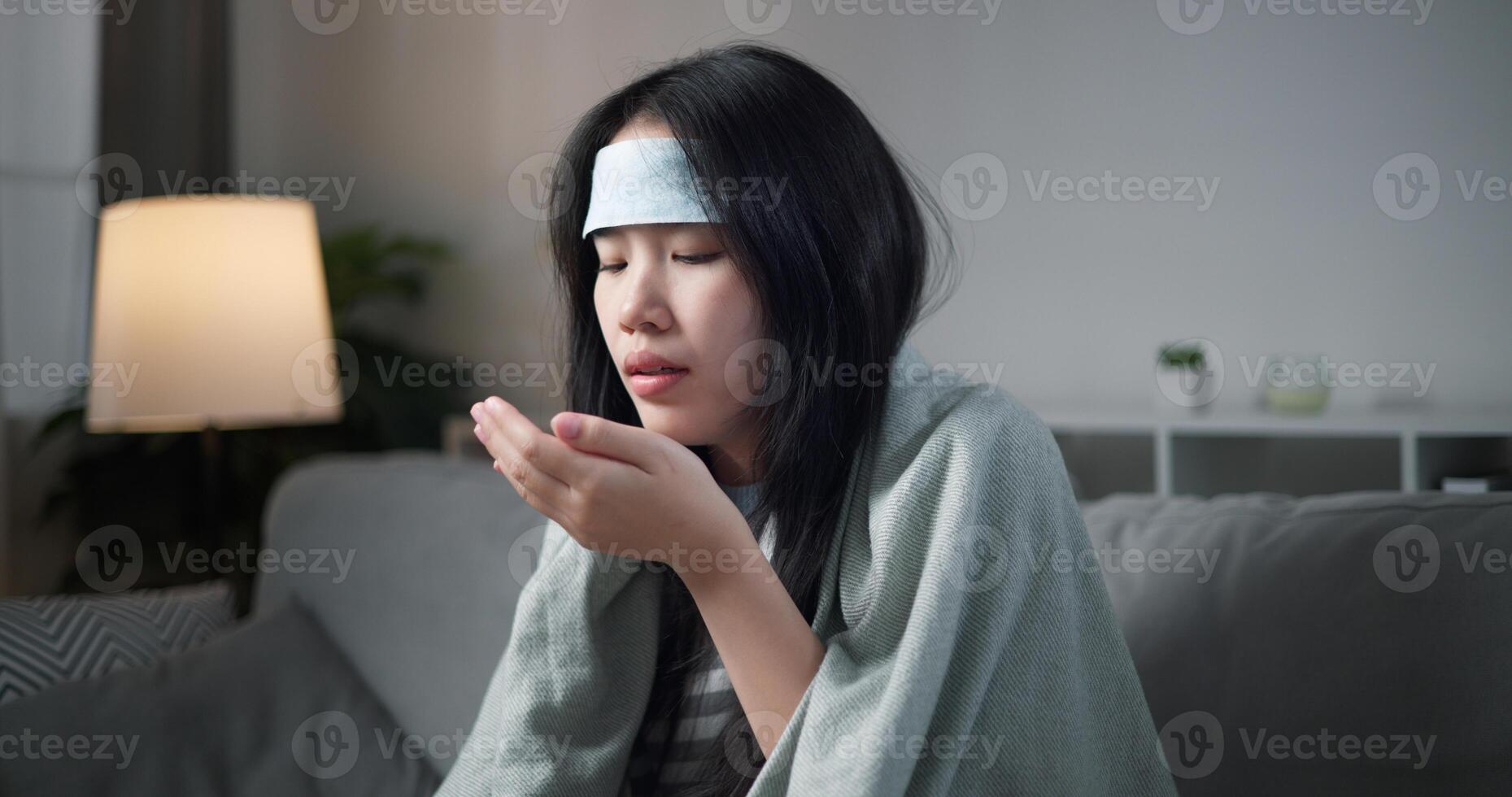 Portrait of Unwell young woman taking pills while have a high fever and ,wrapped in blanket sitting on sofa in the living room at home, healthcare woes photo