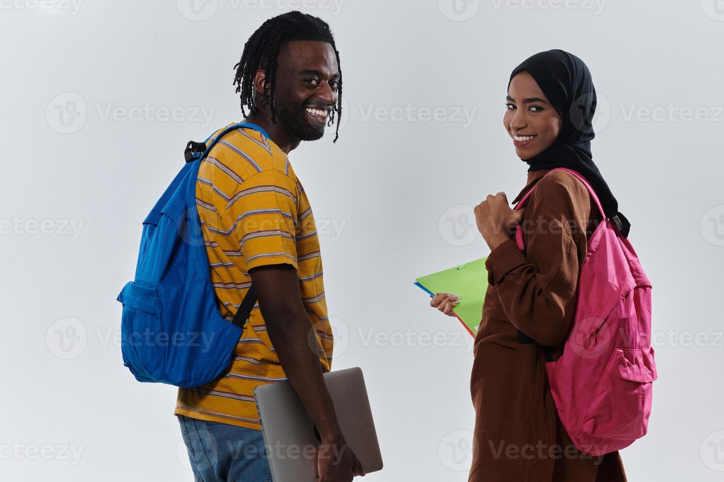 African American student collaborates with his Muslim colleague, who diligently works on her laptop, symbolizing a blend of diversity, modern learning, and cooperative spirit against a serene white photo