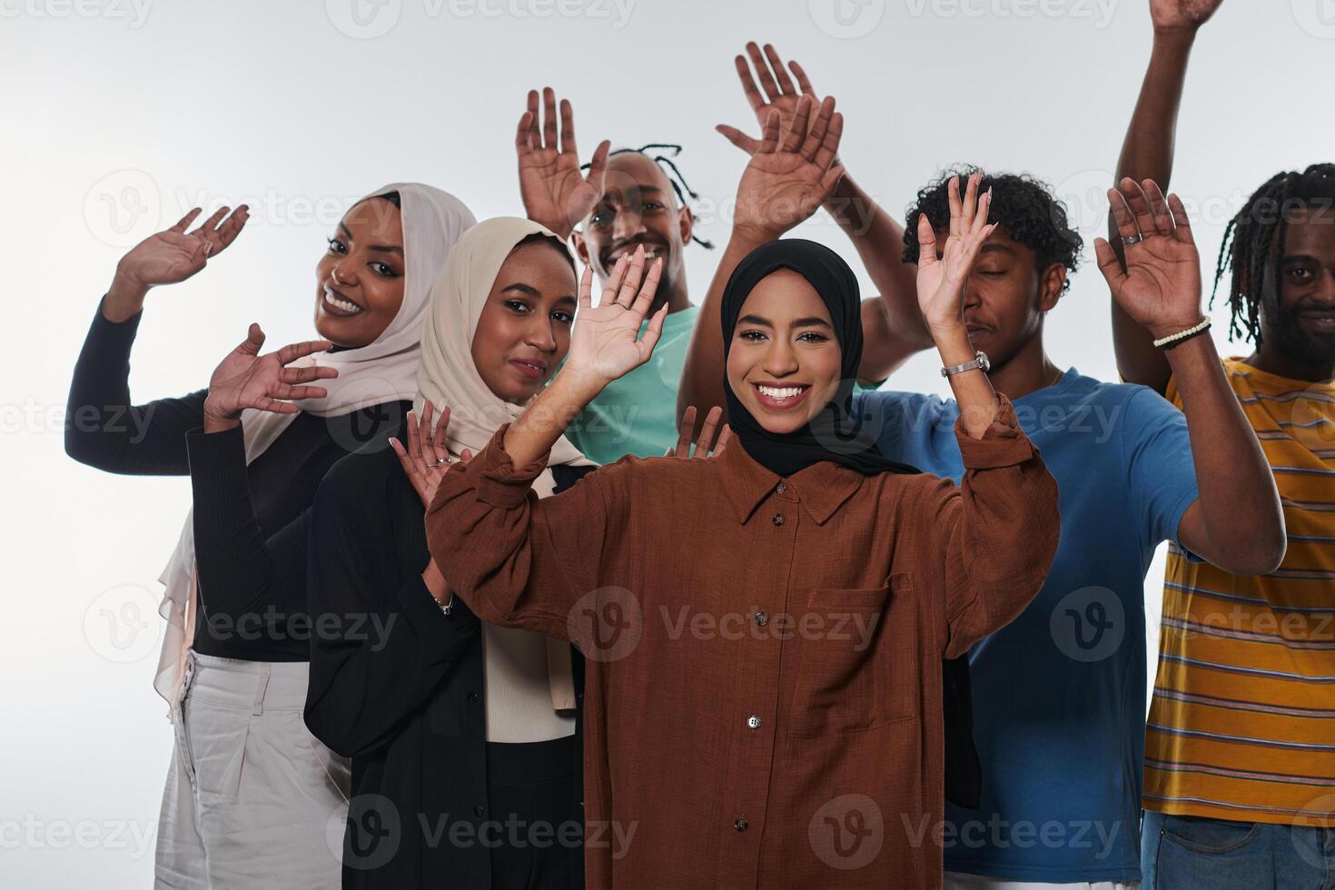 A jubilant and diverse group, including an African American man and hijab-wearing girls, exuberantly wave and celebrate, embodying the vibrancy of student life against a white backdrop, symbolizing photo