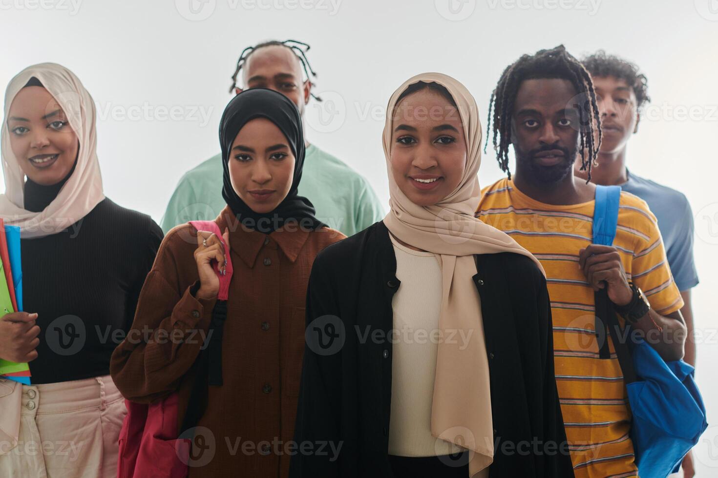 In a vibrant display of educational diversity, a group of students strikes a pose against a clean white background, holding backpacks, laptops, and tablets, symbolizing a blend of modern technology photo