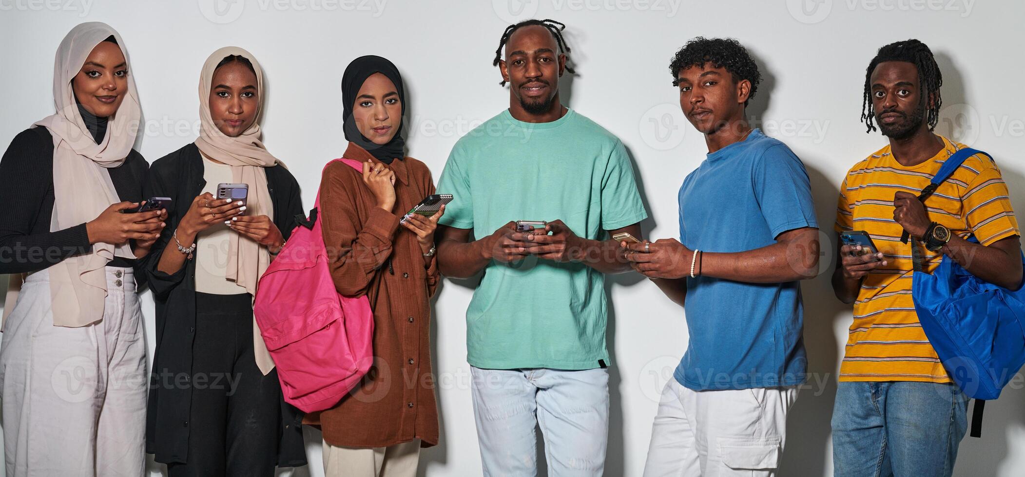 A diverse group of students, immersed in the digital age, stands united while engaging with their smartphones against a white backdrop, symbolizing the modern era of connectivity, communication, and photo