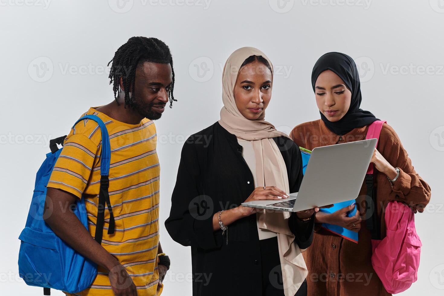 A group of students, including an African American student and two hijab-wearing women, stand united against a pristine white background, symbolizing a harmonious blend of cultures and backgrounds in photo