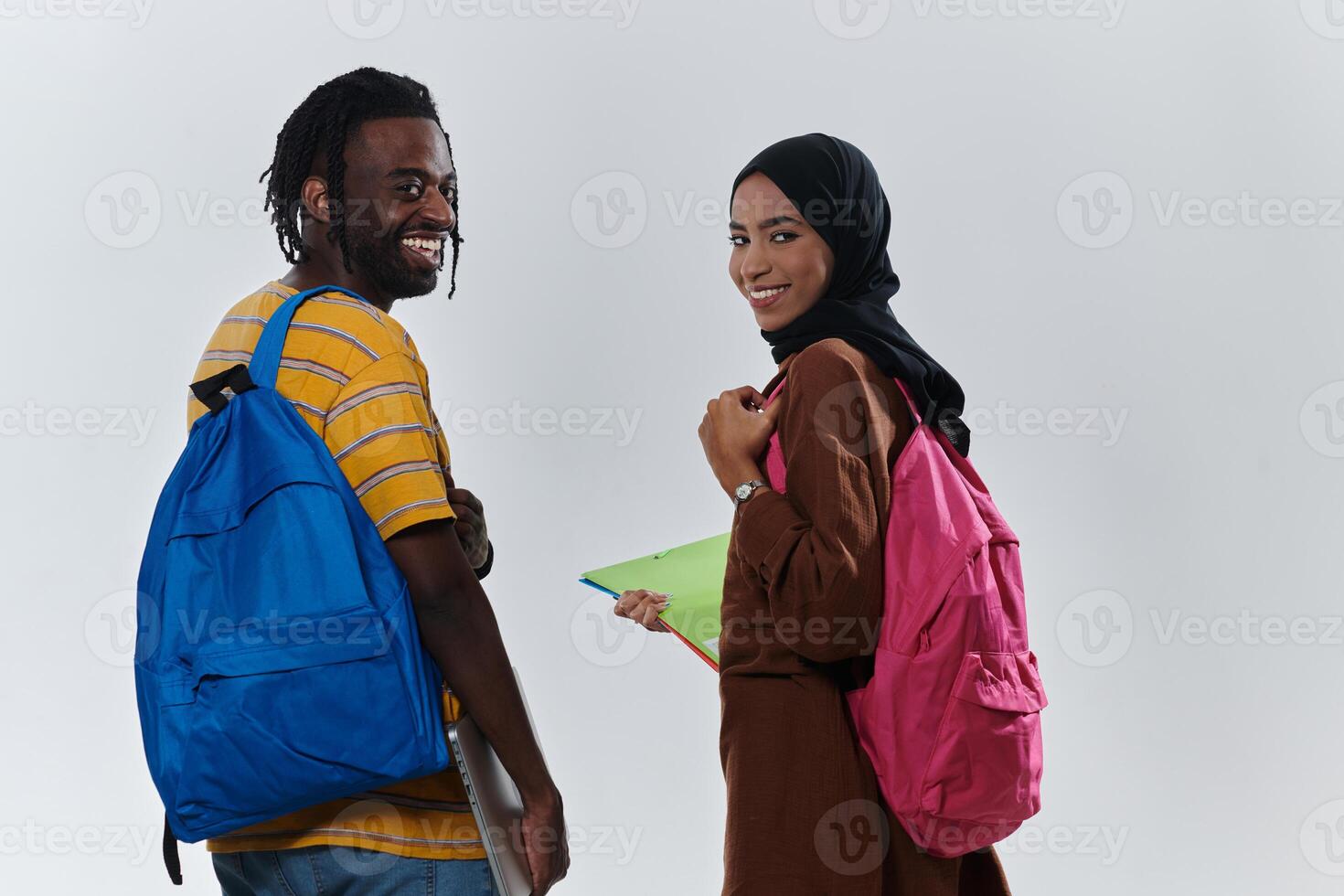 African American student collaborates with his Muslim colleague, who diligently works on her laptop, symbolizing a blend of diversity, modern learning, and cooperative spirit against a serene white photo