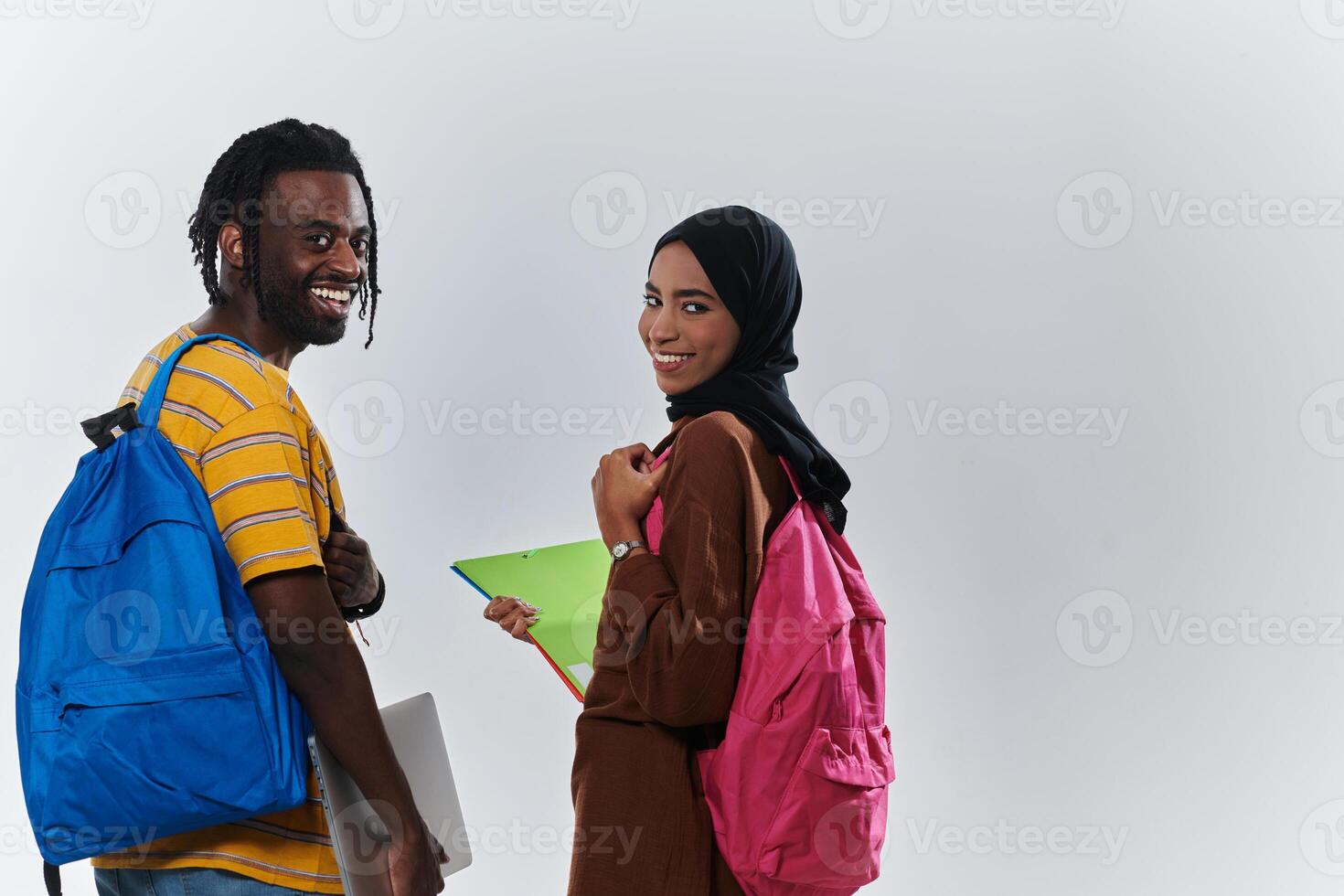 African American student collaborates with his Muslim colleague, who diligently works on her laptop, symbolizing a blend of diversity, modern learning, and cooperative spirit against a serene white photo