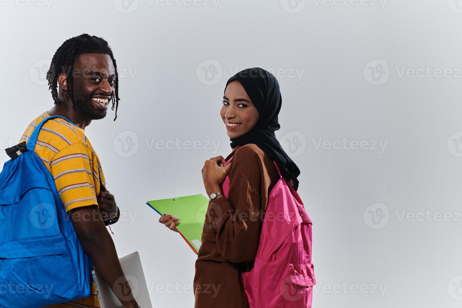 African American student collaborates with his Muslim colleague, who diligently works on her laptop, symbolizing a blend of diversity, modern learning, and cooperative spirit against a serene white photo