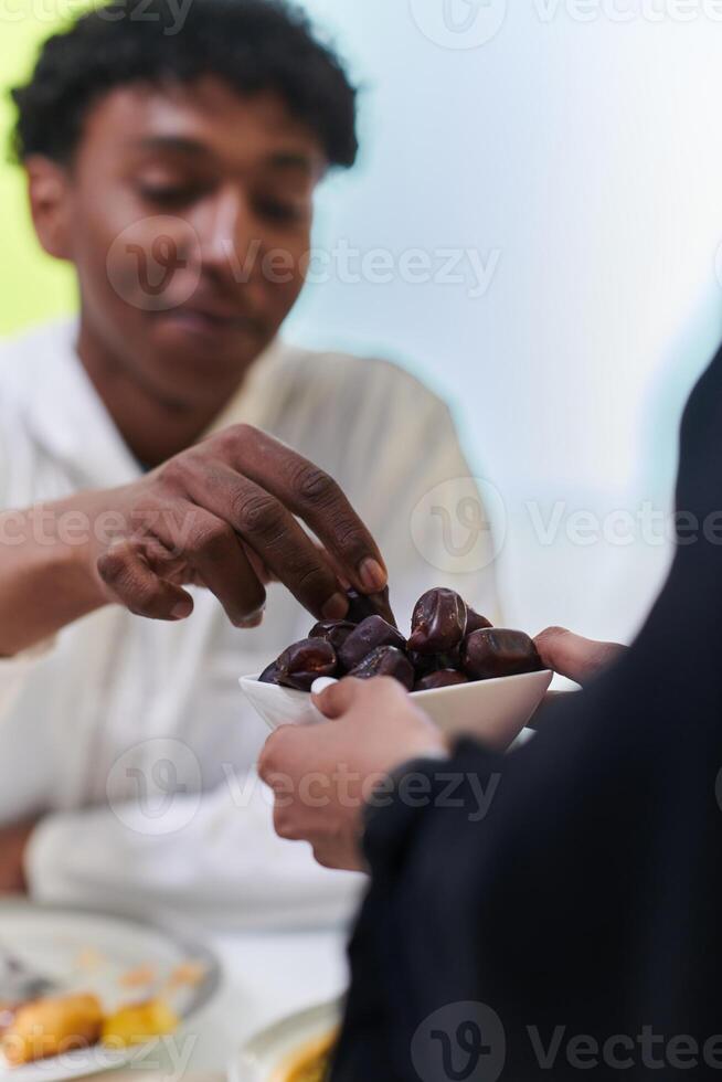 African American Muslim man delicately takes dates to break his fast during the Ramadan month, seated at the family dinner table, embodying a scene of spiritual reflection, cultural tradition, and the photo