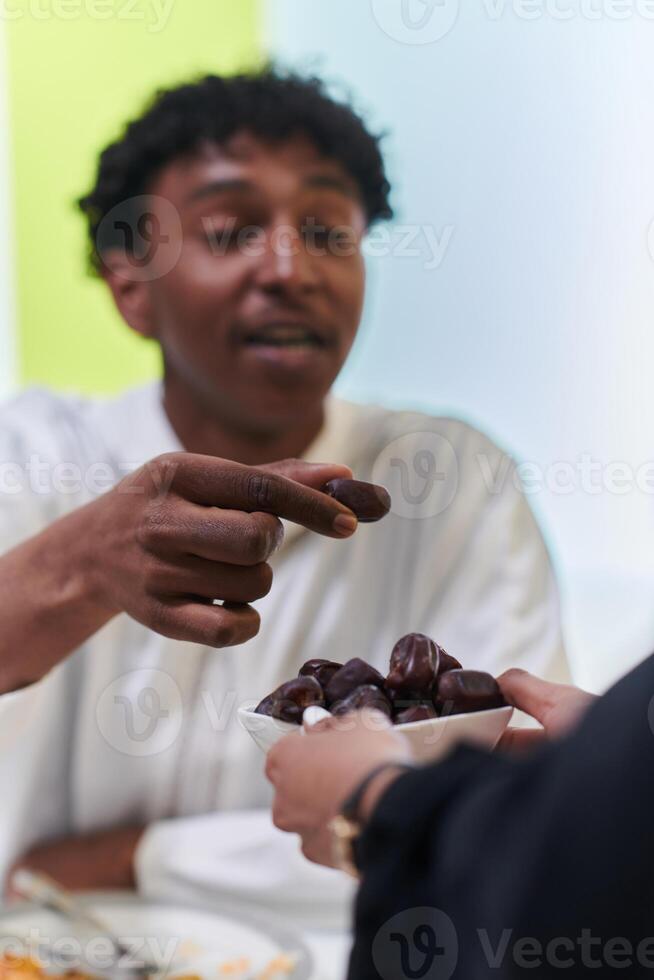 African American Muslim man delicately takes dates to break his fast during the Ramadan month, seated at the family dinner table, embodying a scene of spiritual reflection, cultural tradition, and the photo