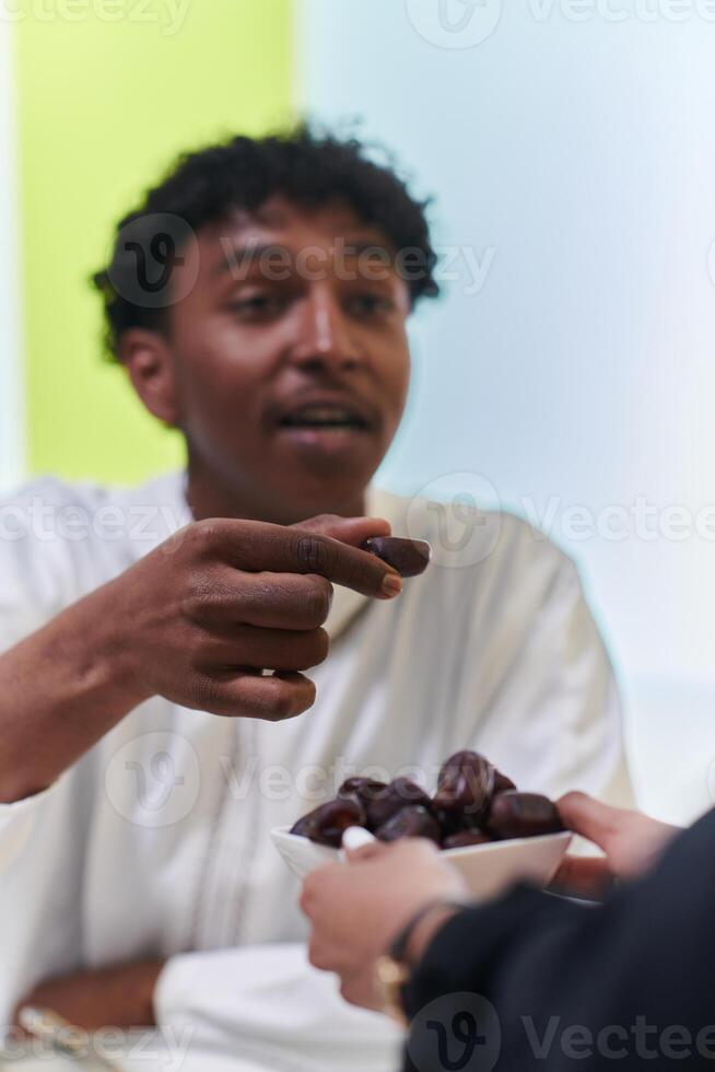 African American Muslim man delicately takes dates to break his fast during the Ramadan month, seated at the family dinner table, embodying a scene of spiritual reflection, cultural tradition, and the photo
