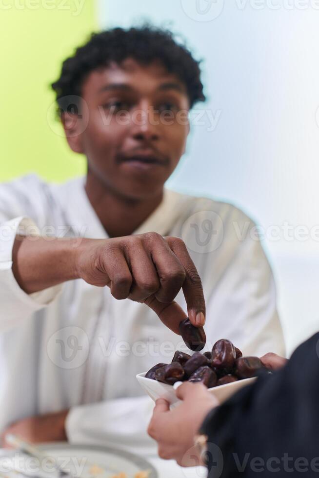 African American Muslim man delicately takes dates to break his fast during the Ramadan month, seated at the family dinner table, embodying a scene of spiritual reflection, cultural tradition, and the photo