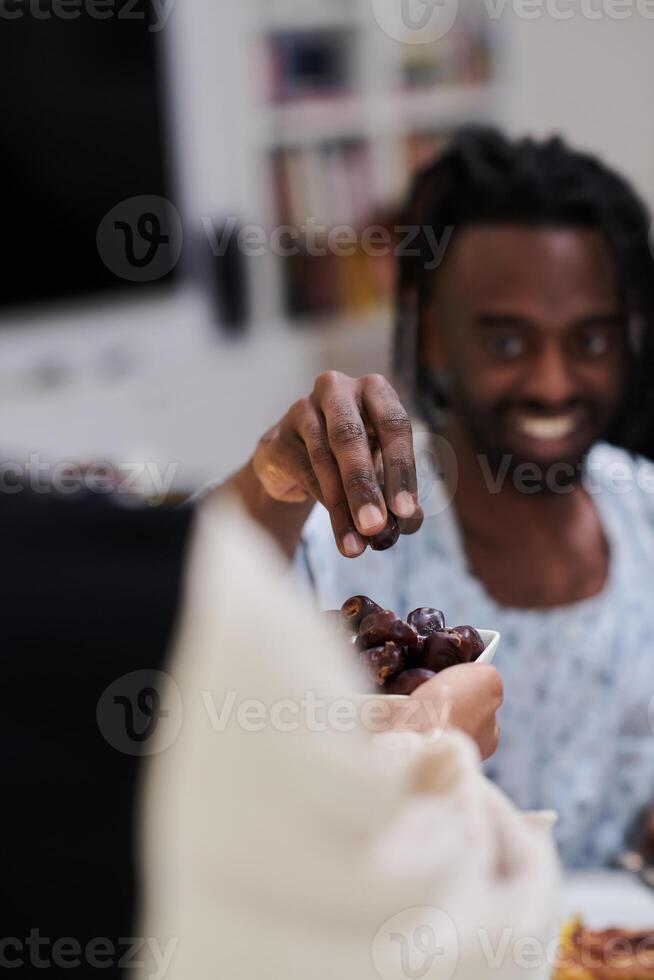 African American Muslim man delicately takes dates to break his fast during the Ramadan month, seated at the family dinner table, embodying a scene of spiritual reflection, cultural tradition, and the photo