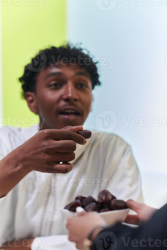 African American Muslim man delicately takes dates to break his fast during the Ramadan month, seated at the family dinner table, embodying a scene of spiritual reflection, cultural tradition, and the photo