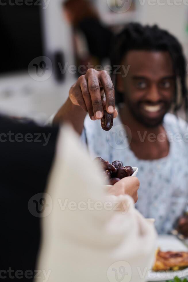 African American Muslim man delicately takes dates to break his fast during the Ramadan month, seated at the family dinner table, embodying a scene of spiritual reflection, cultural tradition, and the photo