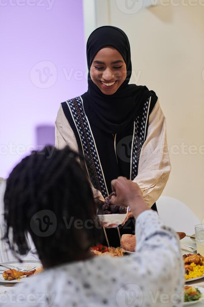 In a heartwarming scene during the sacred month of Ramadan, a traditional Muslim woman offers dates to her family gathered around the table, exemplifying the spirit of unity, generosity, and cultural photo