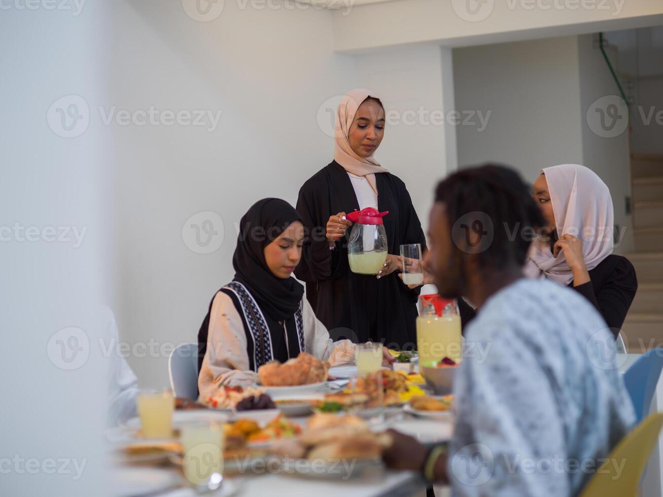 A diverse Islamic family gathers for iftar, joyfully breaking their fast together during Ramadan, with a Muslim woman in a beautiful hijab gracefully pouring water to mark the end of their fast photo
