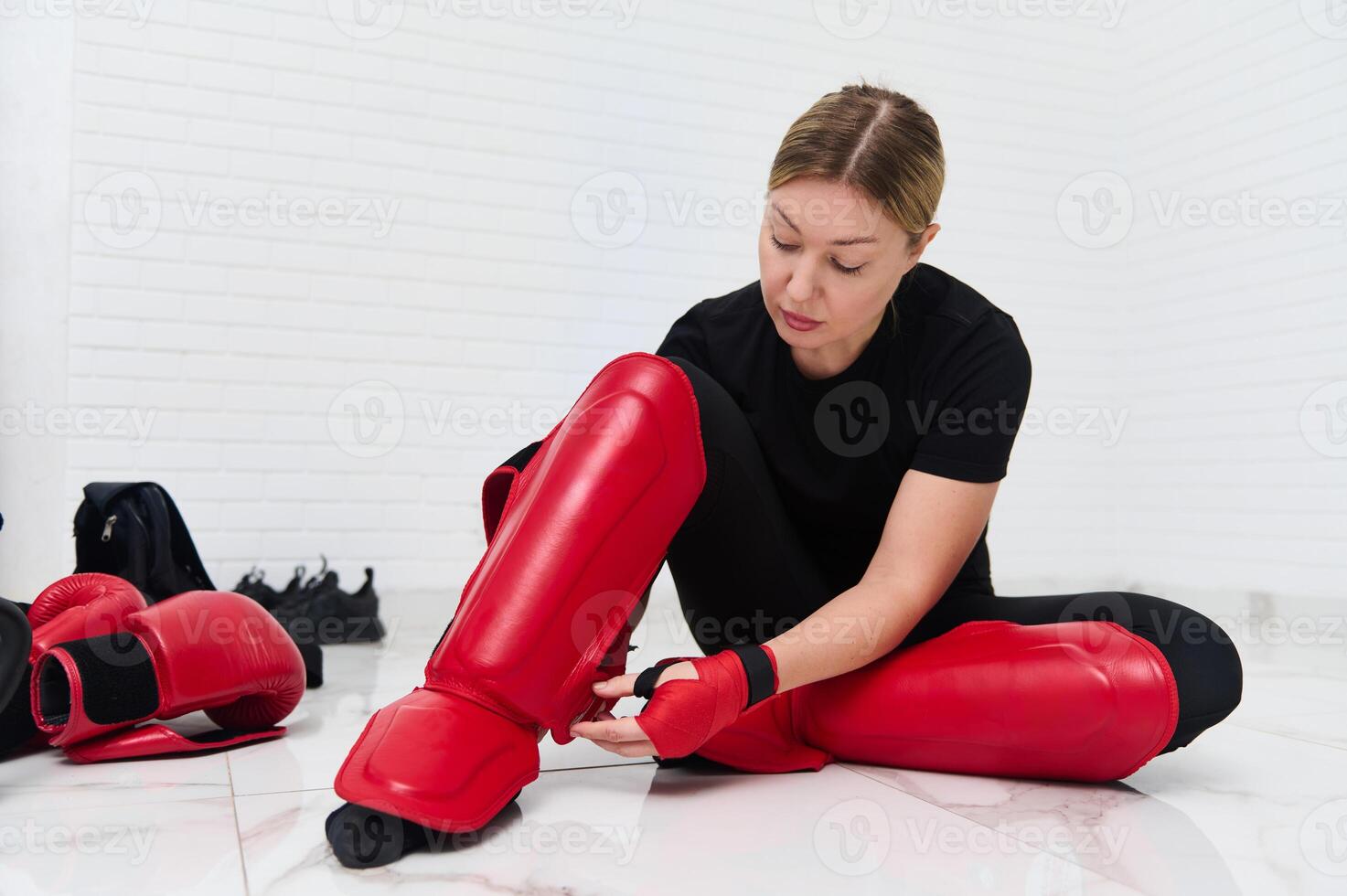 Full size shot of female fighter kickboxer, putting on red protective kickboxing equipment on legs, ready for training, isolated over white background. People. Kickboxing workout. Martial art photo