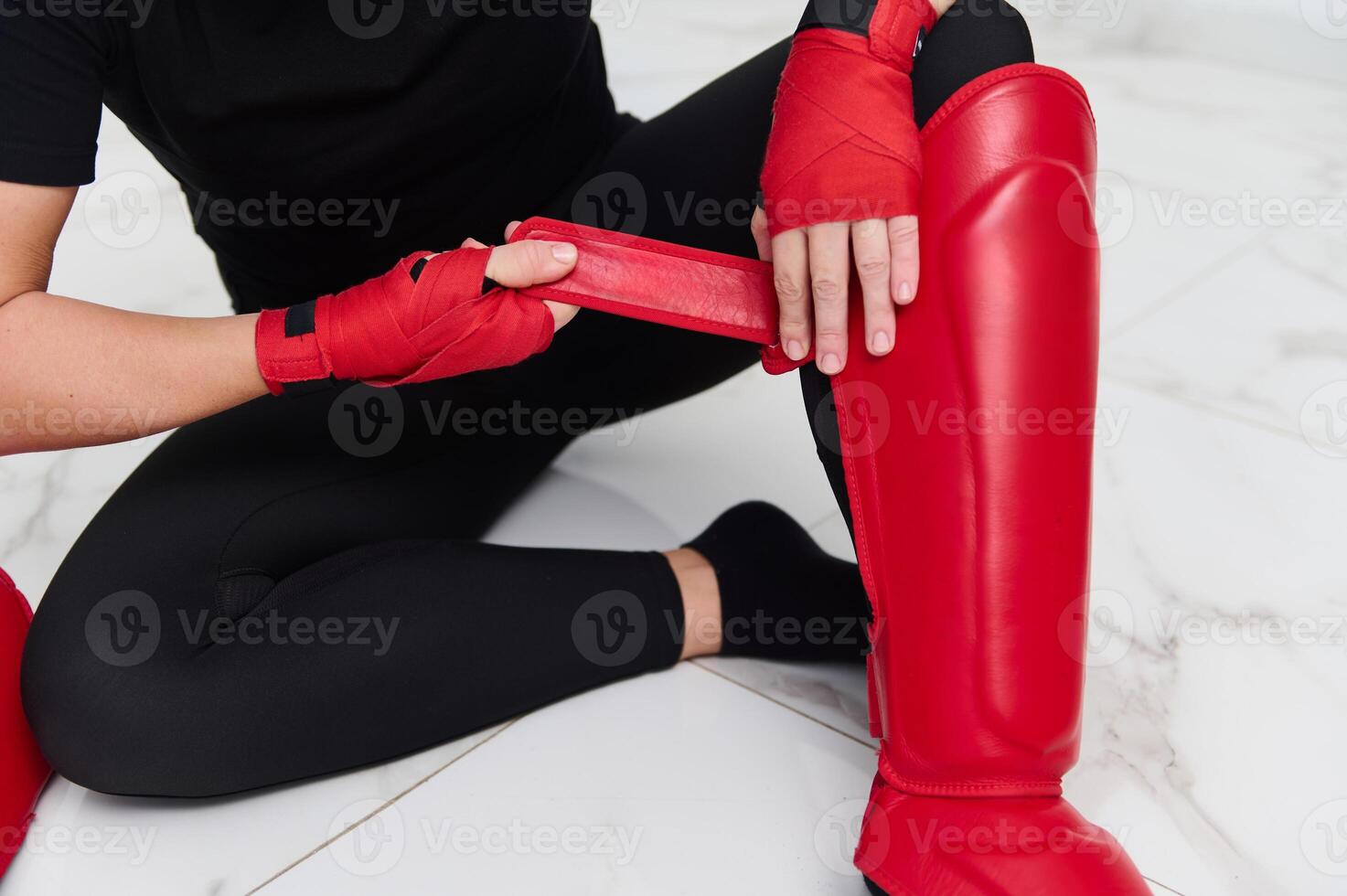Selective focus on legs of a woman boxer fighter putting on red kickboxing leg pads guard. Sparring shin guards. Martial art, combat, challenge. Kickboxing concept. photo